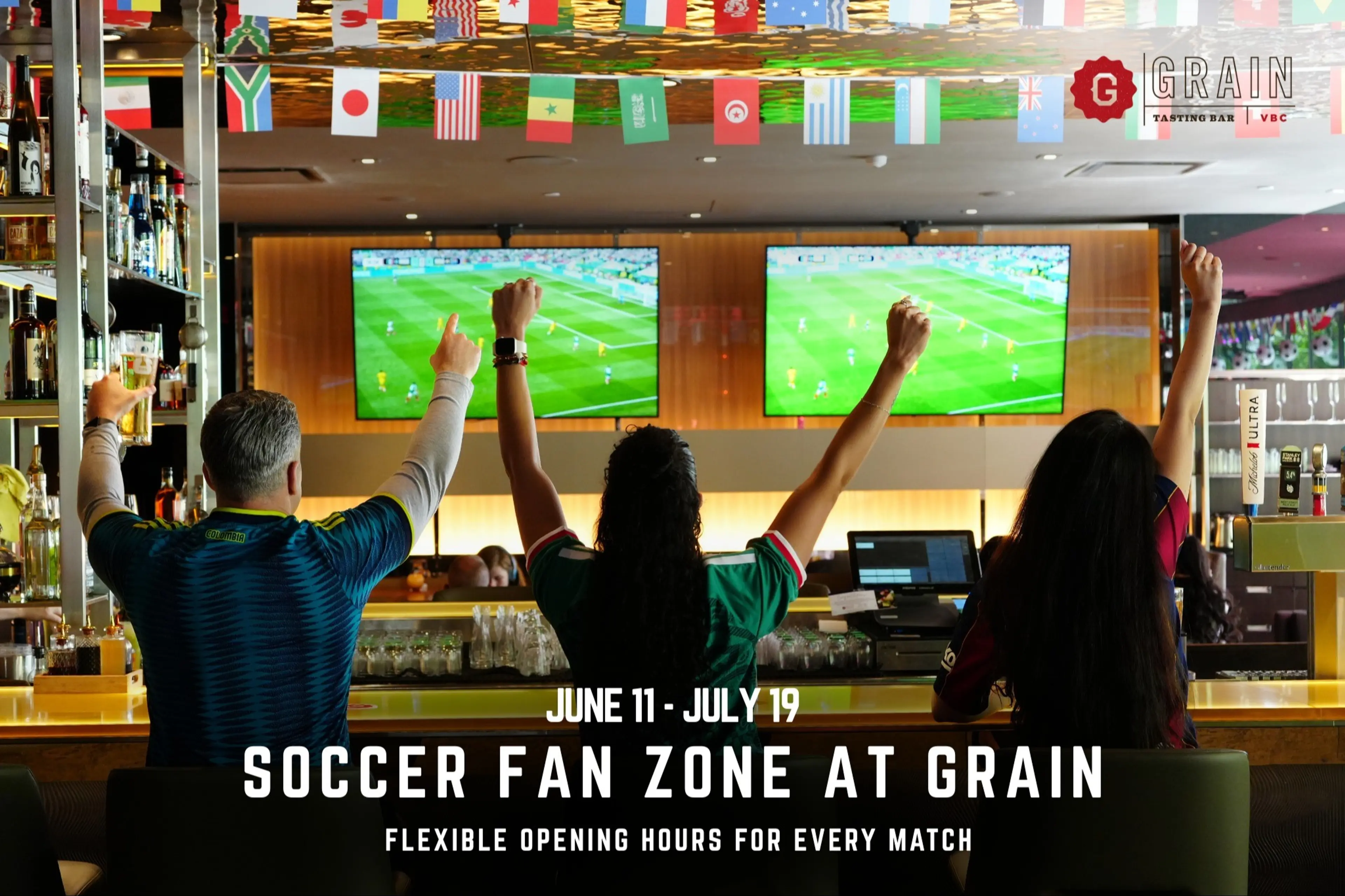 Three people raising arms cheering while watching soccer on two TV screens in a bar decorated with international flags.