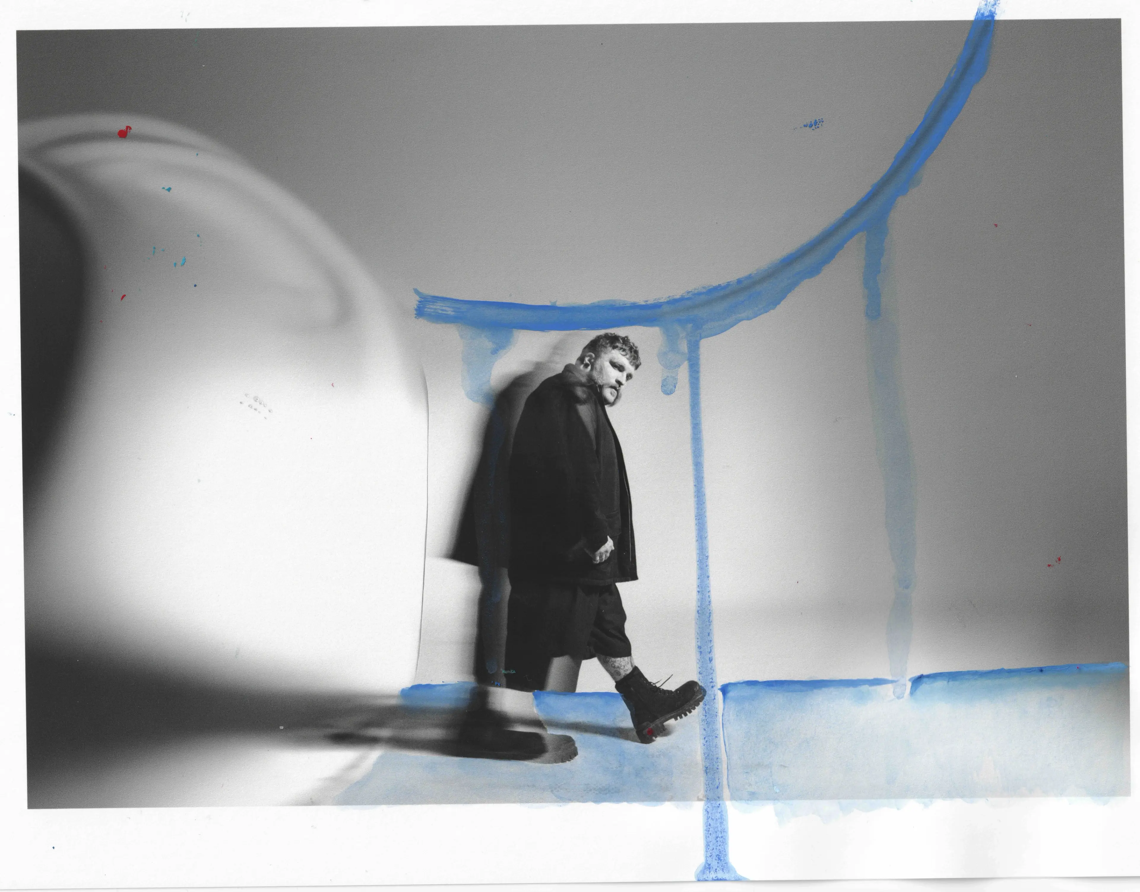 Person in dark clothing walking with one foot raised, casting a shadow on a wall with blue paint streaks.
