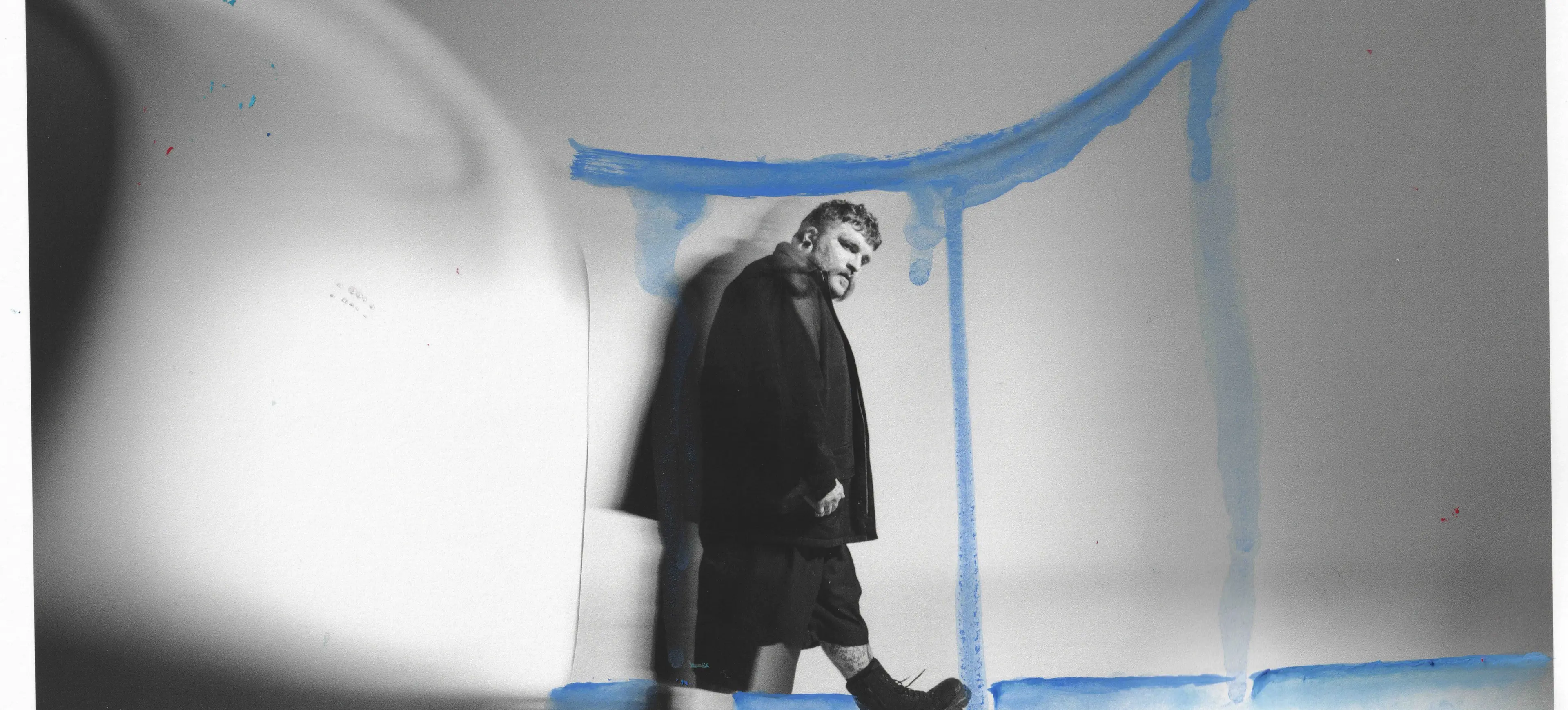 Person in dark clothing walking with one foot raised, casting a shadow on a wall with blue paint streaks.