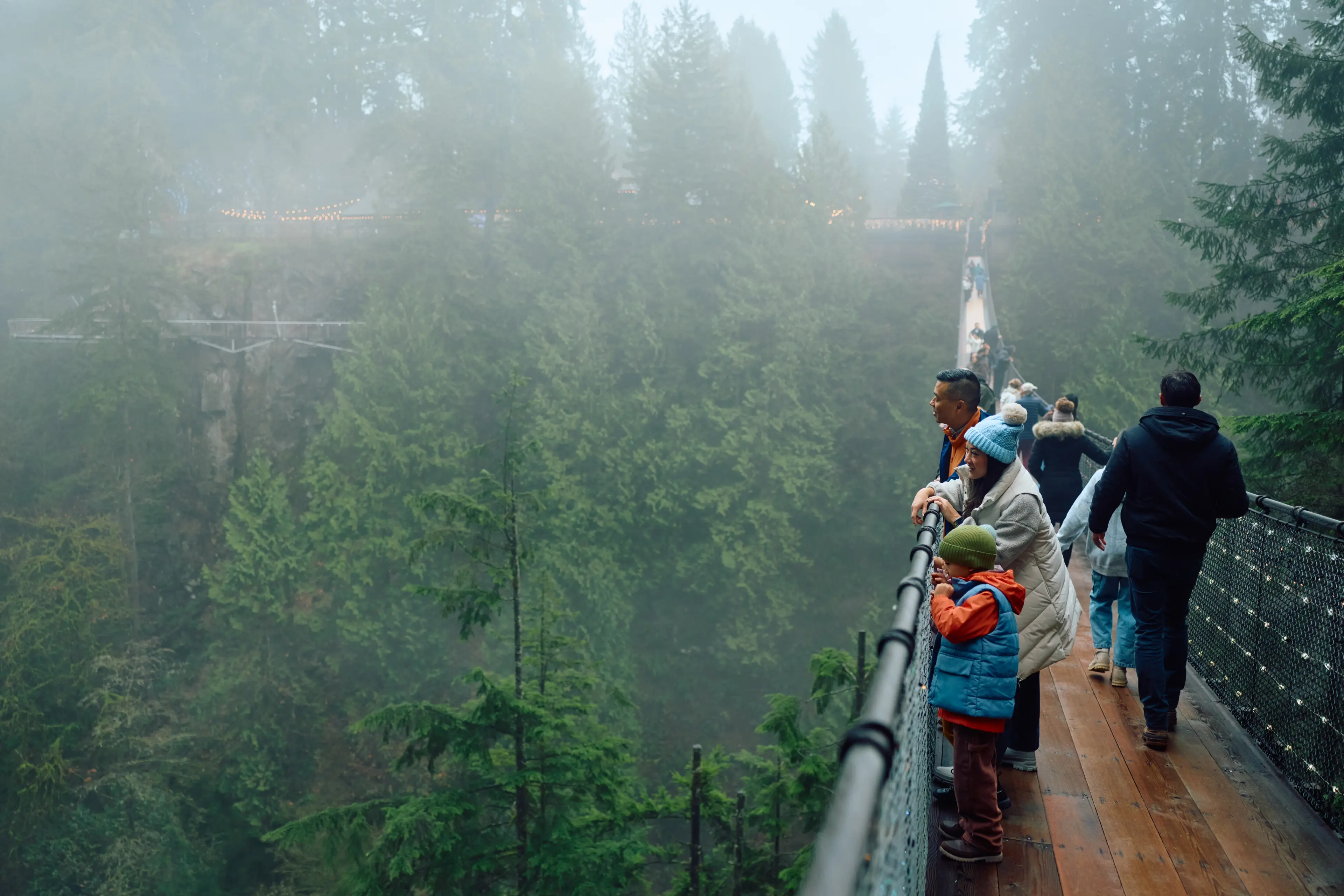 A family with two kids on the Capilano Suspension Bridge on a foggy day in North Vancouver.
