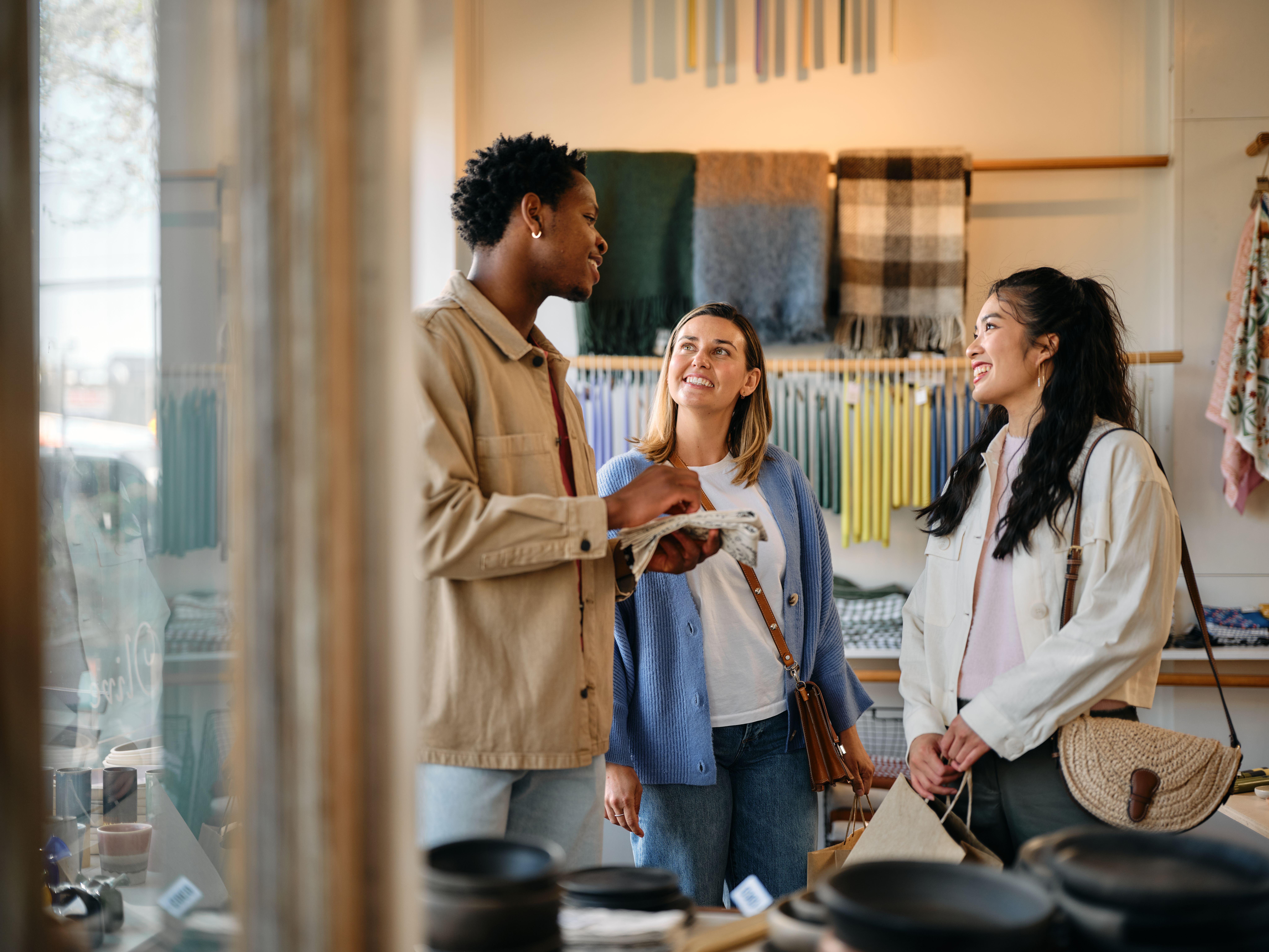 Three people smiling and talking inside a store with textiles and pottery on display.