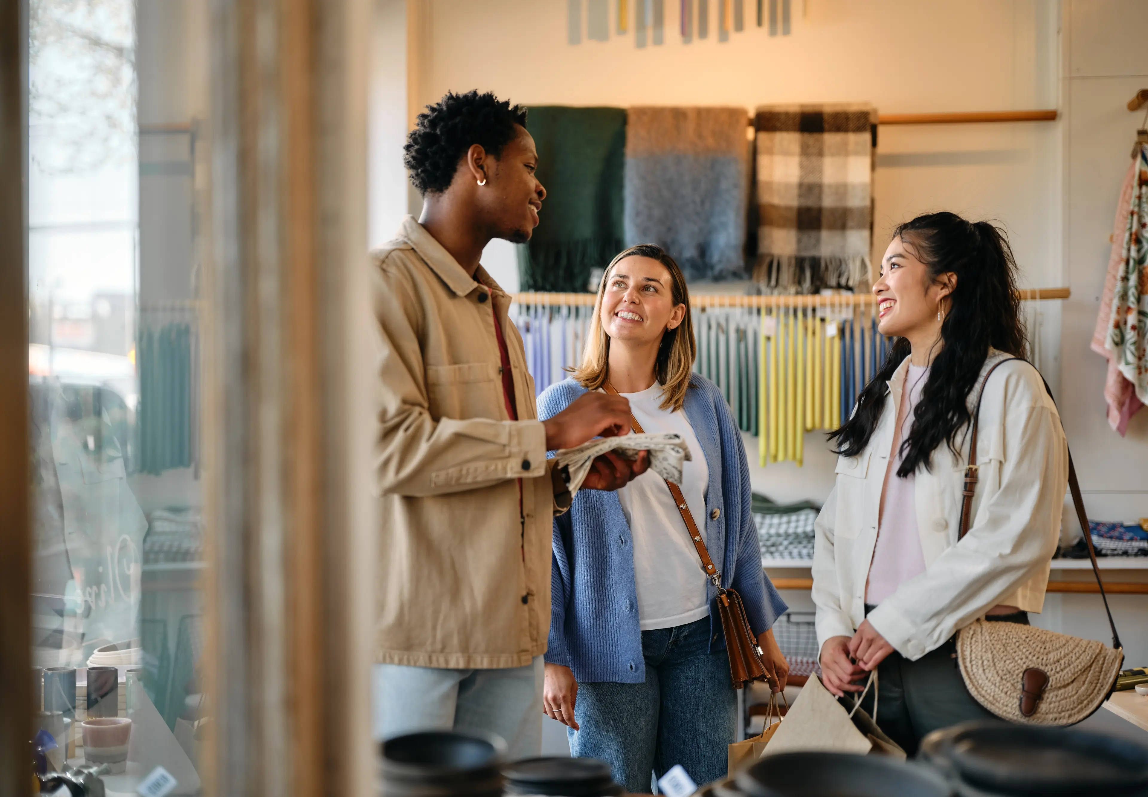 Three people smiling and talking inside a store with textiles and pottery on display.