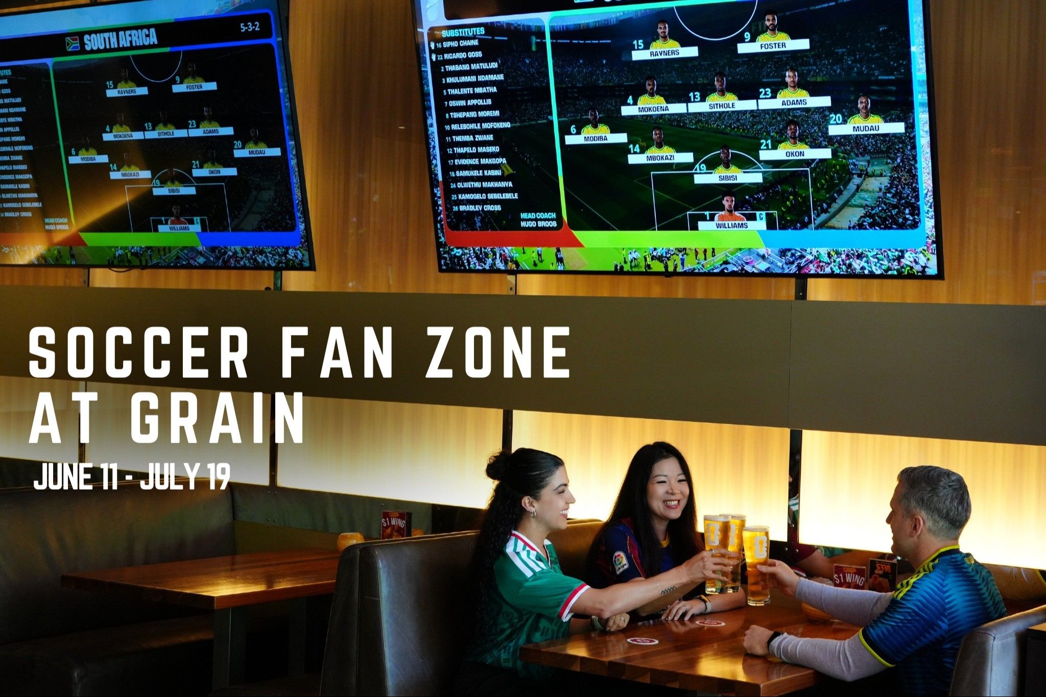 Three people sitting at a table in a sports bar, clinking glasses of beer, with two large screens showing soccer team lineups above them.