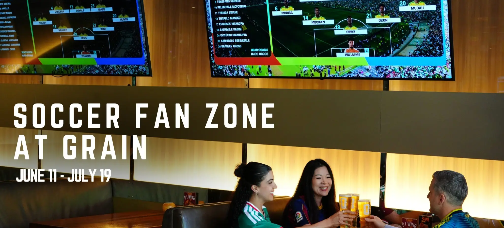 Three people sitting at a table in a sports bar, clinking glasses of beer, with two large screens showing soccer team lineups above them.
