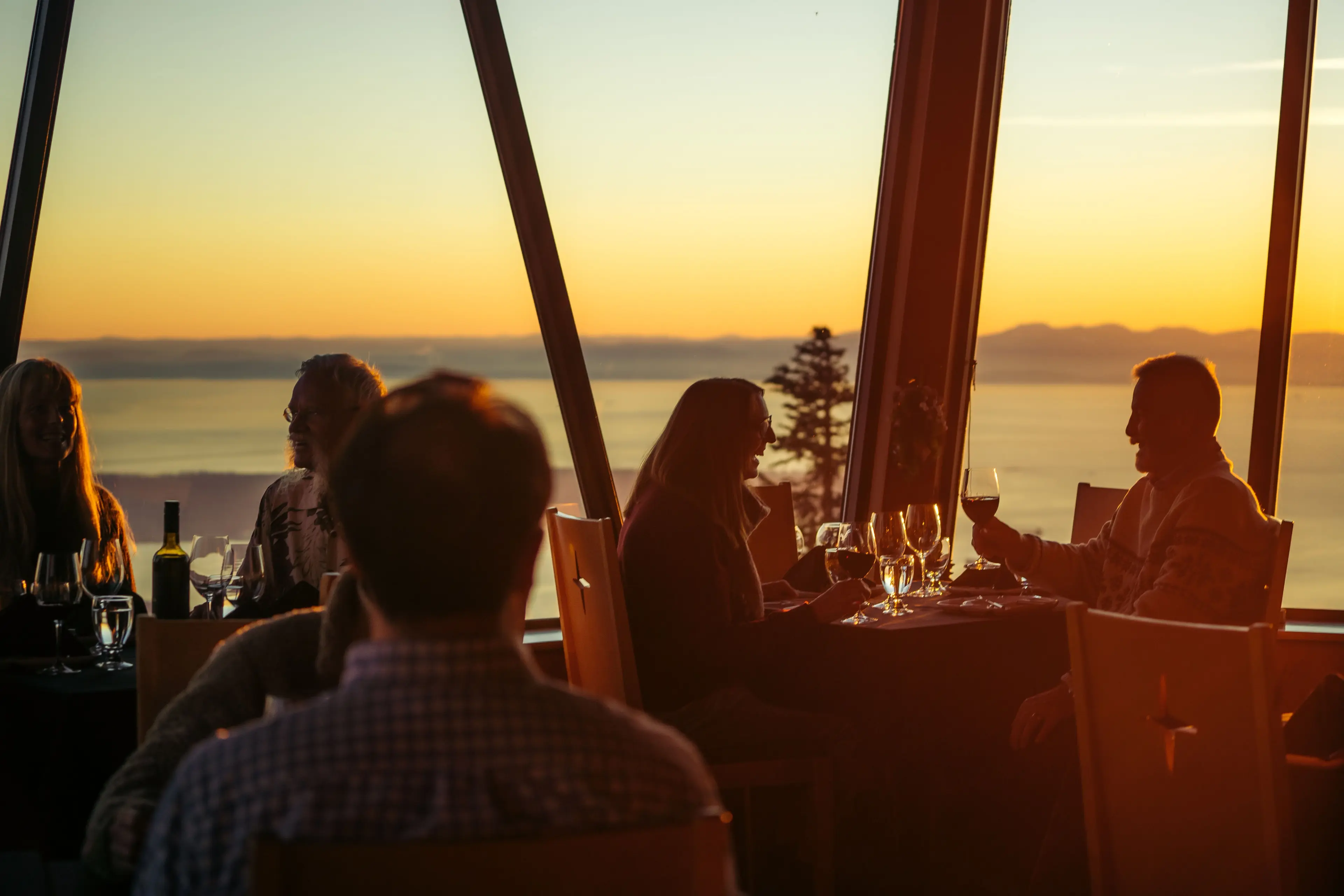 Tables of people dine at the Observatory at Grouse Mountain. You can see the sunset through the large windows. 