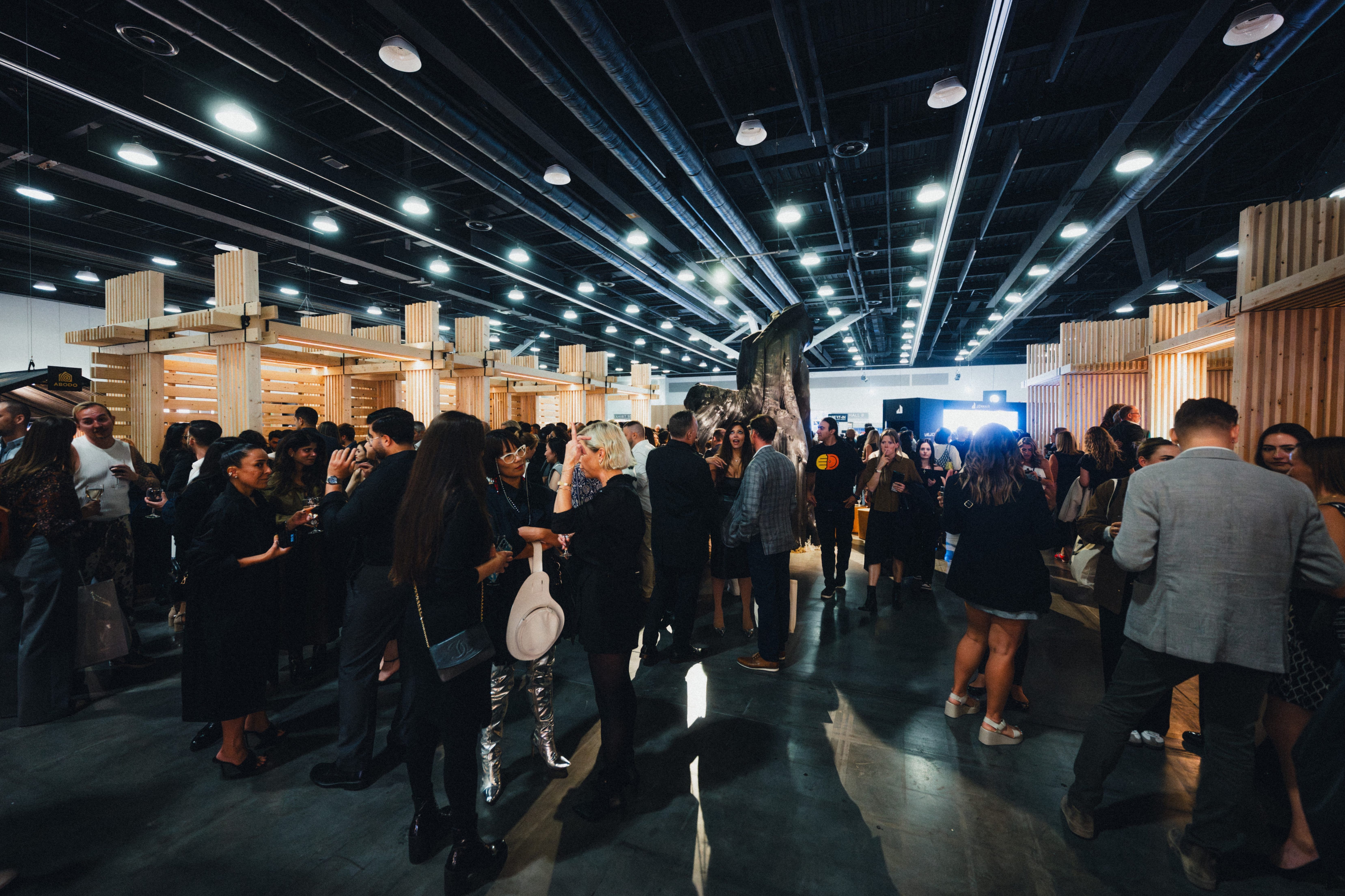 Crowd of people socializing in a large indoor event space with wooden structures and bright ceiling lights.