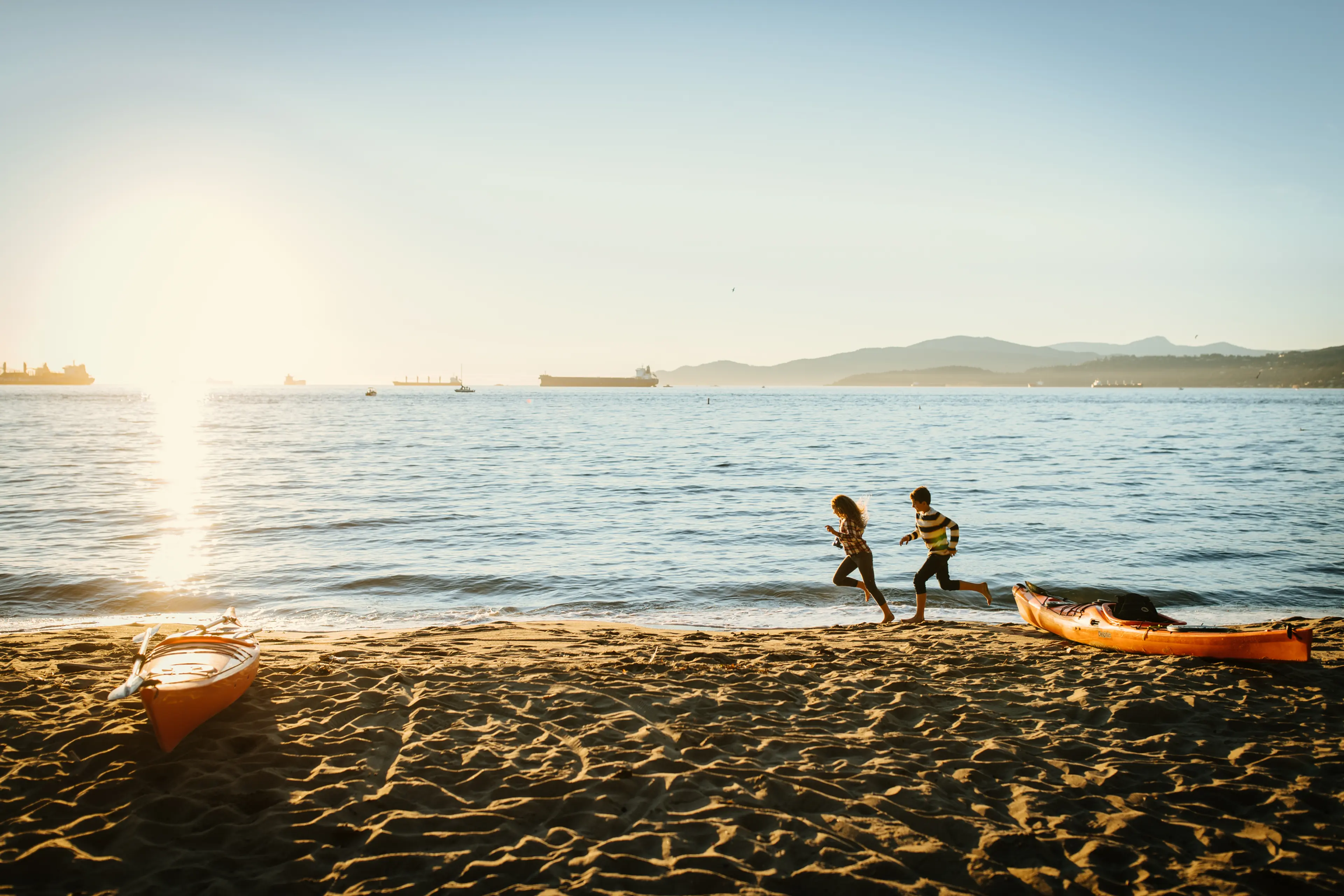 Kids running on Third Beach with kayaks.