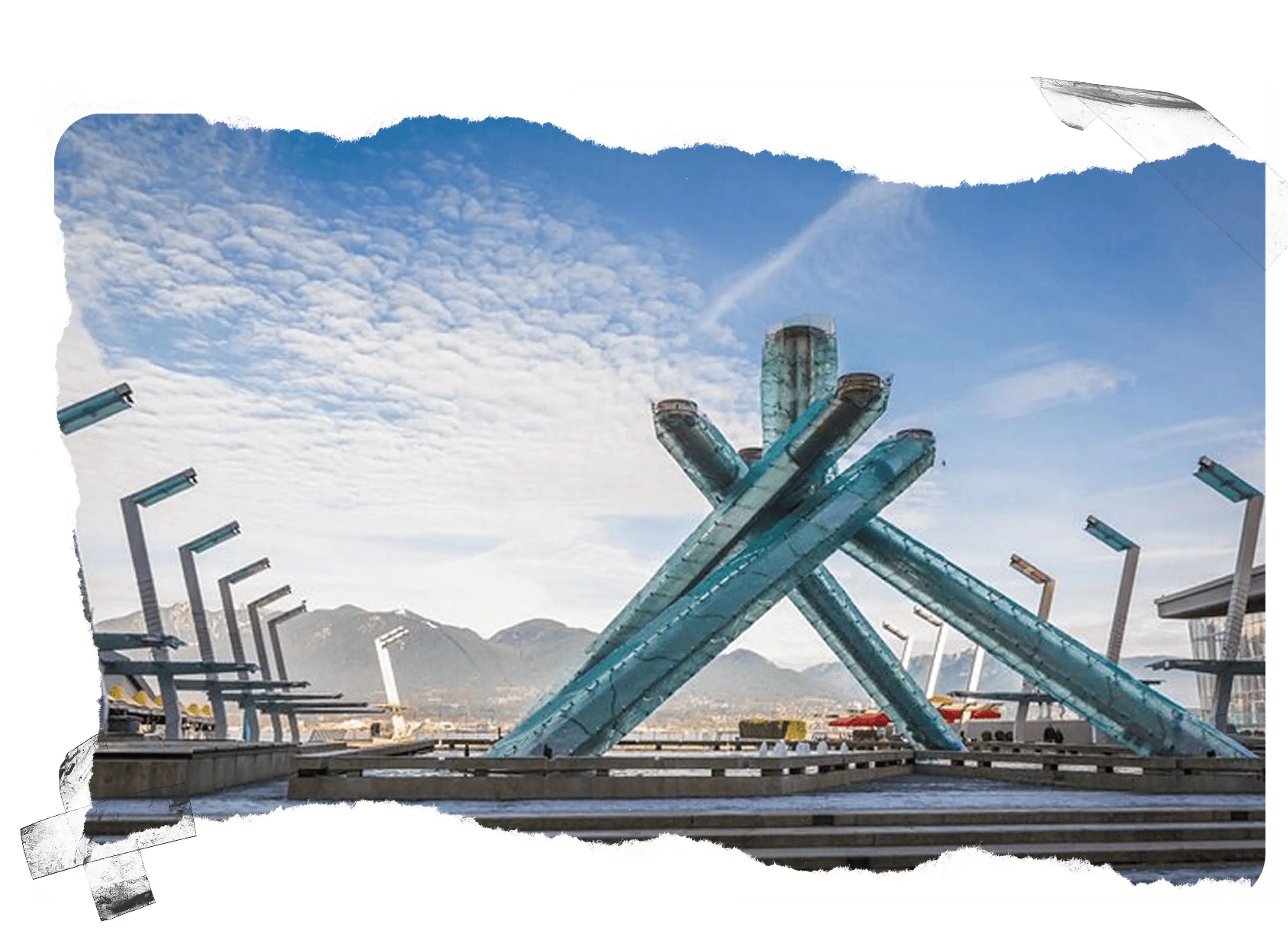 Large blue glass Olympic cauldron sculpture with mountains and cloudy sky in the background.