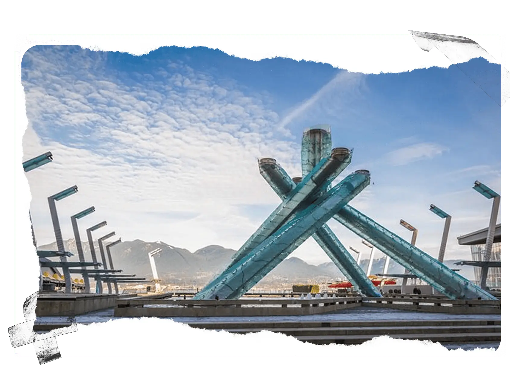 Large blue glass Olympic cauldron sculpture with mountains and cloudy sky in the background.