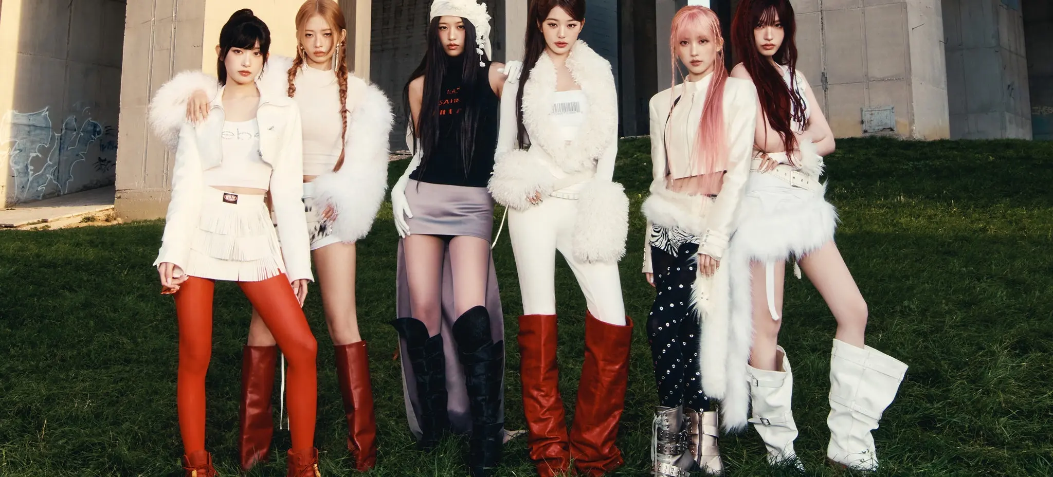 Six people standing on grass in front of a concrete structure, wearing stylish outfits with boots and fur accents.