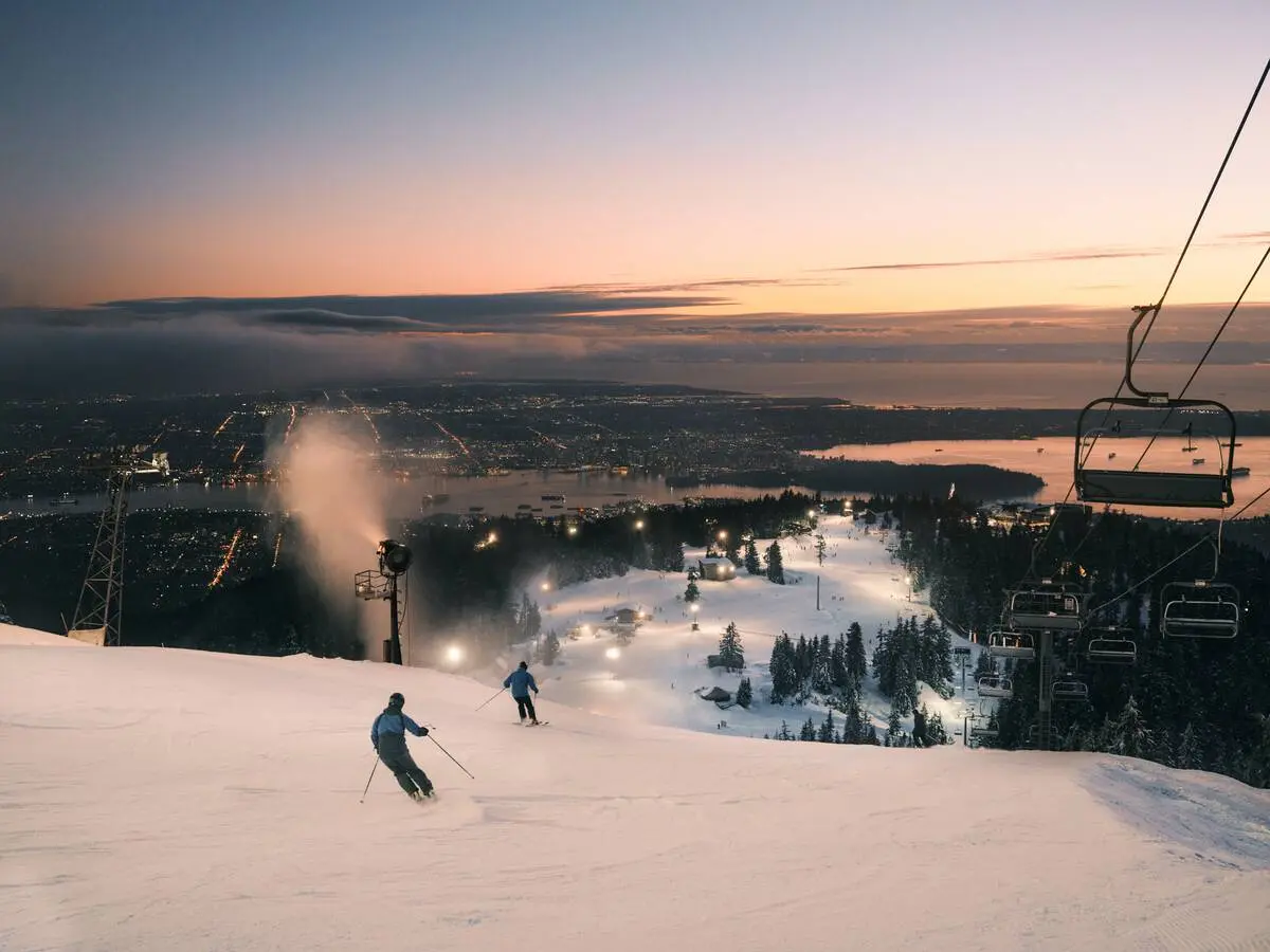 Skiers at Grouse Mountain ski under floodlights with the lights of Vancouver below them
