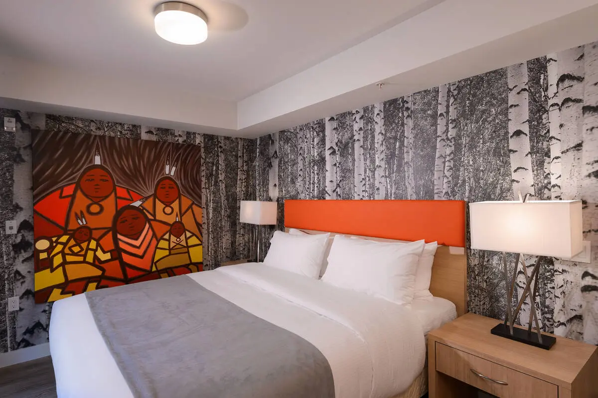 One of the rooms at Skwachays Lodge in Vancouver. The walls have birch tree wall paper and a large colourful painting of an Indigenous familya