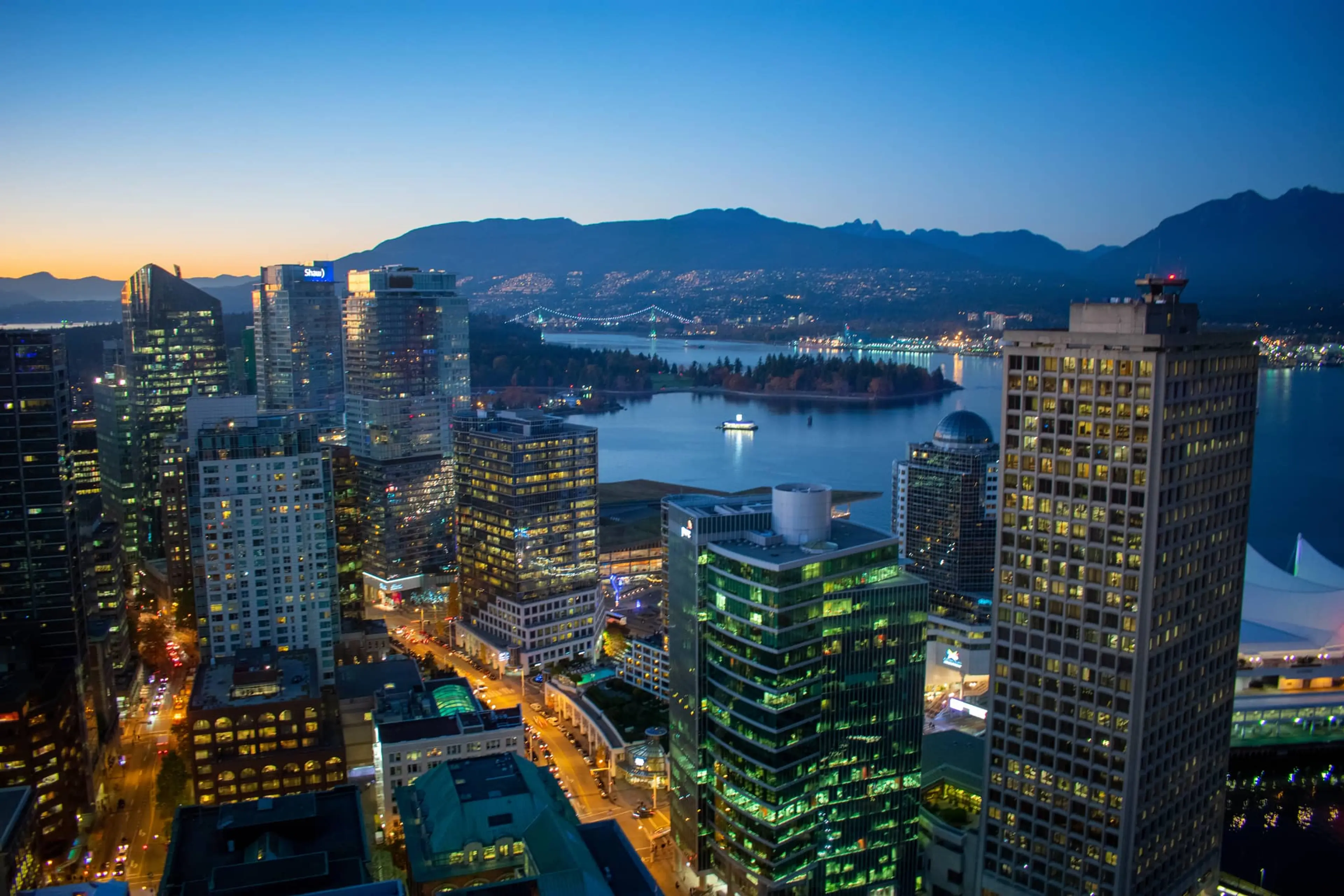 An arial shot of Vancouver lit up at night. A large river and the mountains behind.
