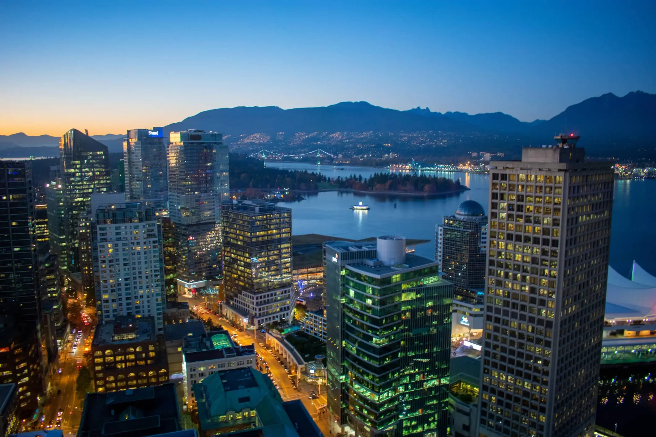 An arial shot of Vancouver lit up at night. A large river and the mountains behind.