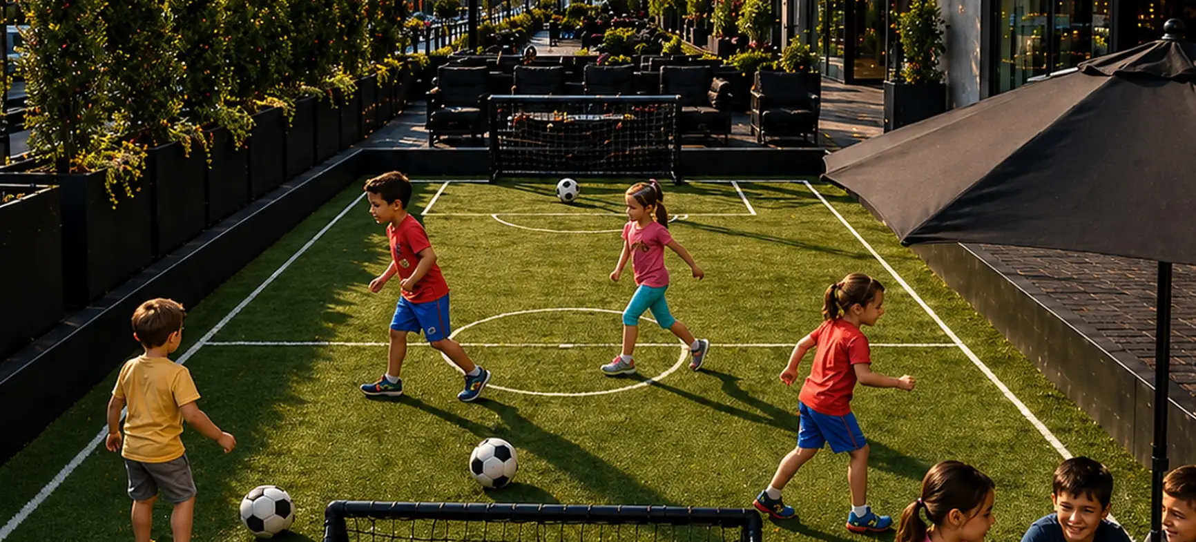 Children playing soccer on a small rooftop field while others sit at tables under string lights in an urban setting.