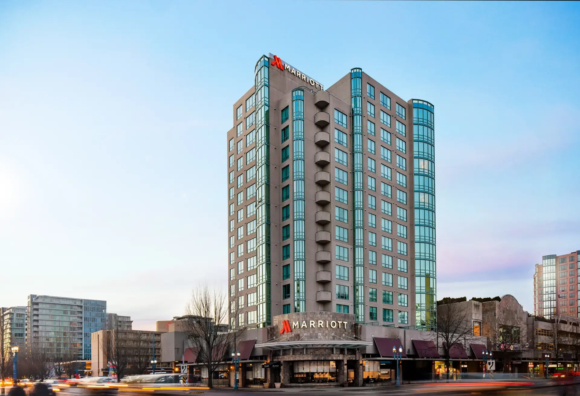 Tall Marriott hotel building with glass windows and balconies at dusk in an urban area with light trails from passing cars.