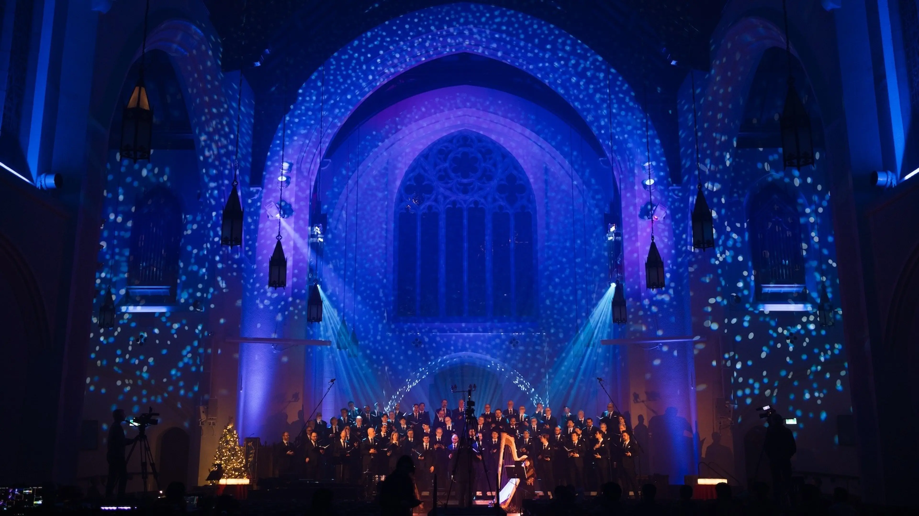 Choir performing in a church with blue and purple lighting and snowflake projections on walls and arches.