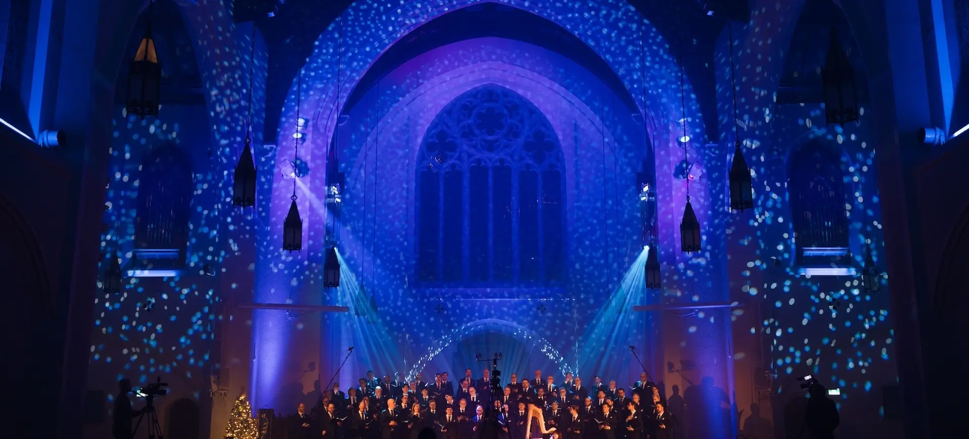 Choir performing in a church with blue and purple lighting and snowflake projections on walls and arches.