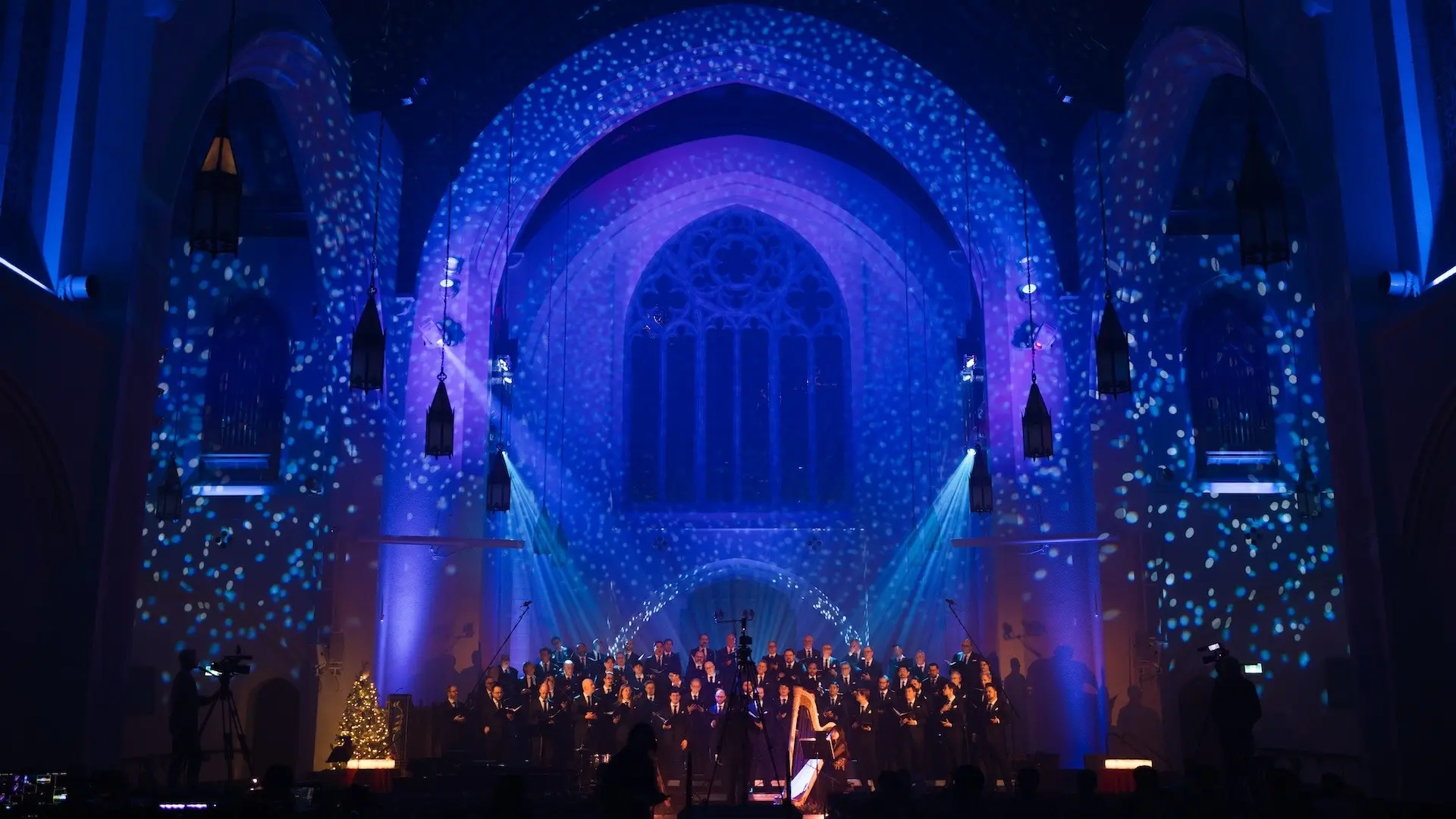 Choir performing in a church with blue and purple lighting and snowflake projections on walls and arches.