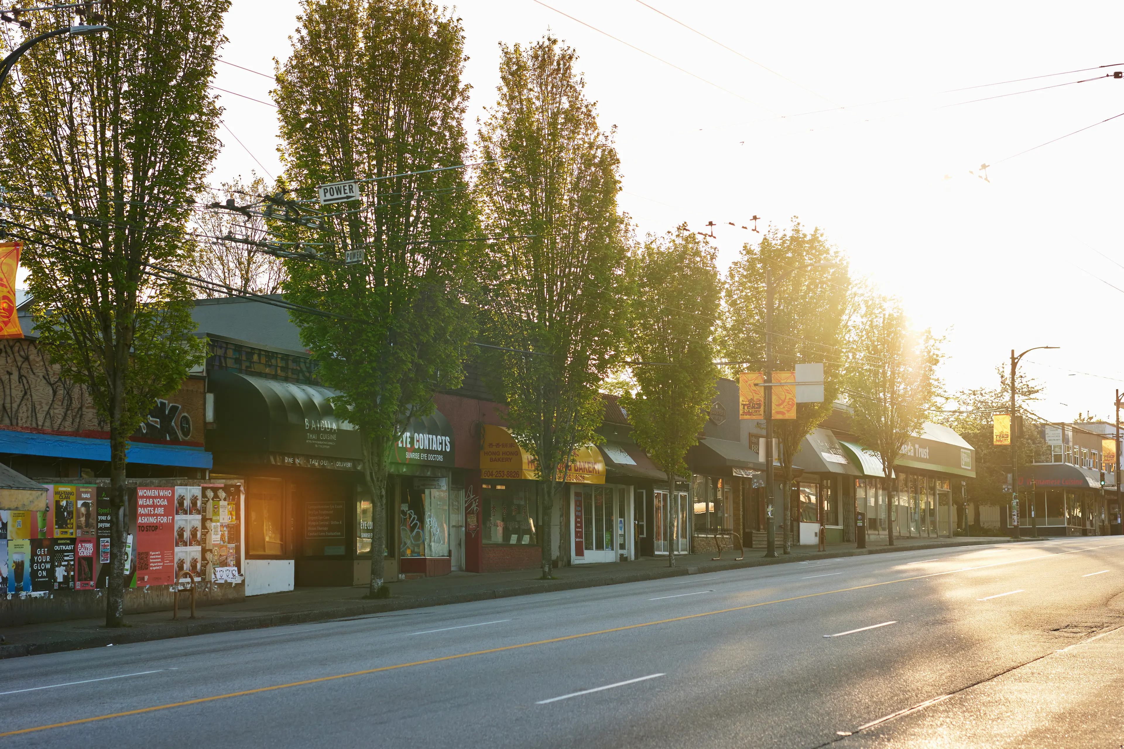 East Village street view with small shops and tall trees on the sidewalk during bright sunset.