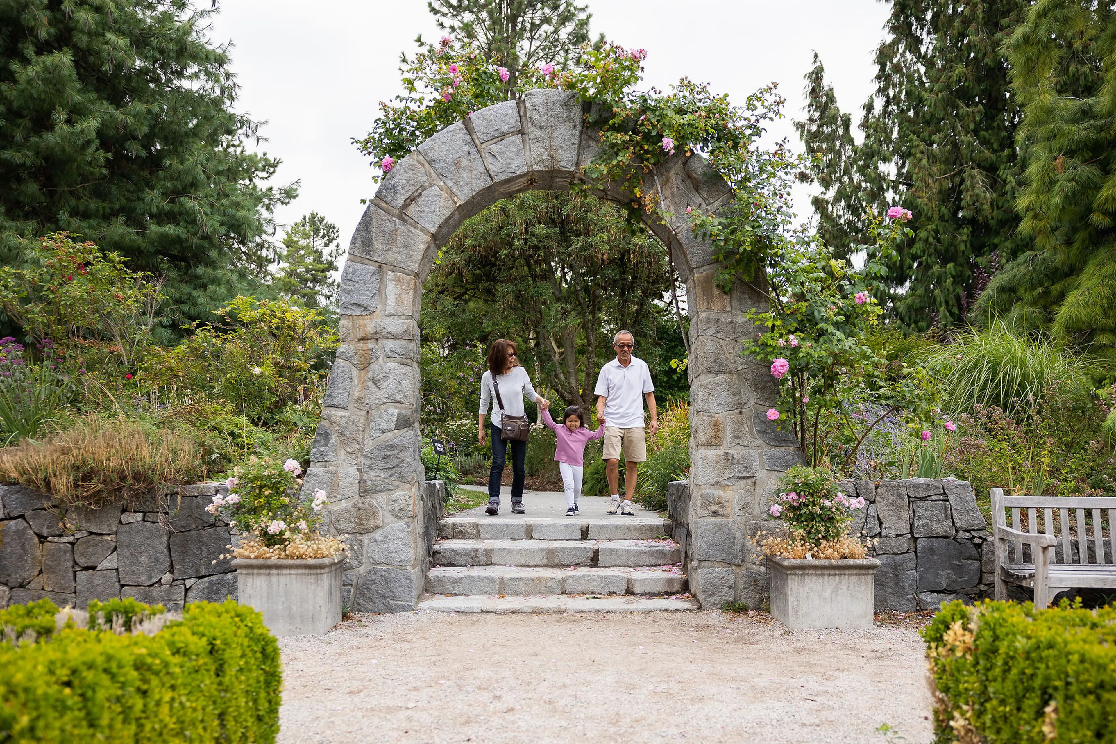 Grandparents and a granddaughter walk through a stone arch at VanDusen Botanical Garden. 