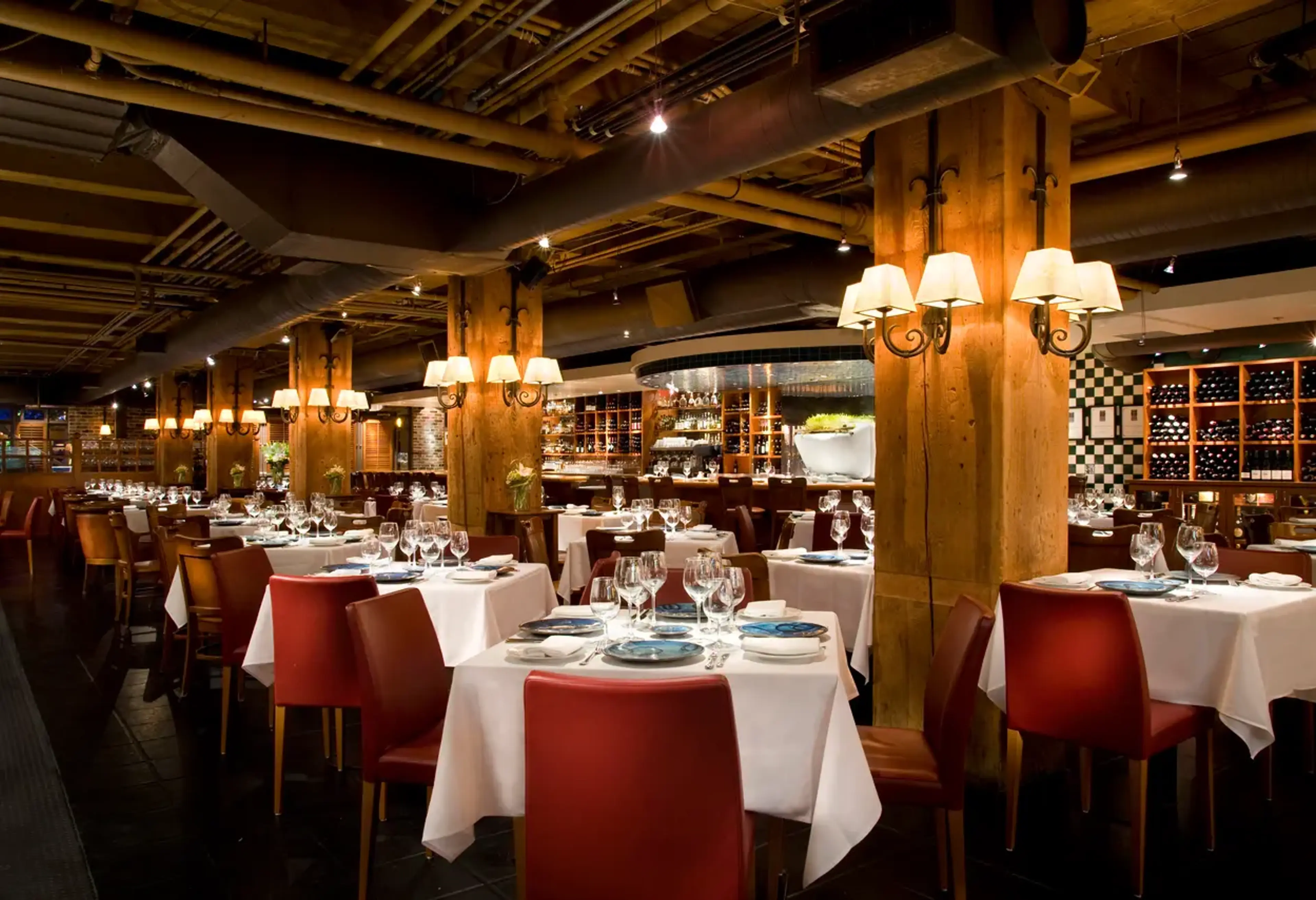 Upscale restaurant interior with wooden beams, tablecloths, chairs, and warm wall lamps at the Blue Water Cafe in Vancouver..