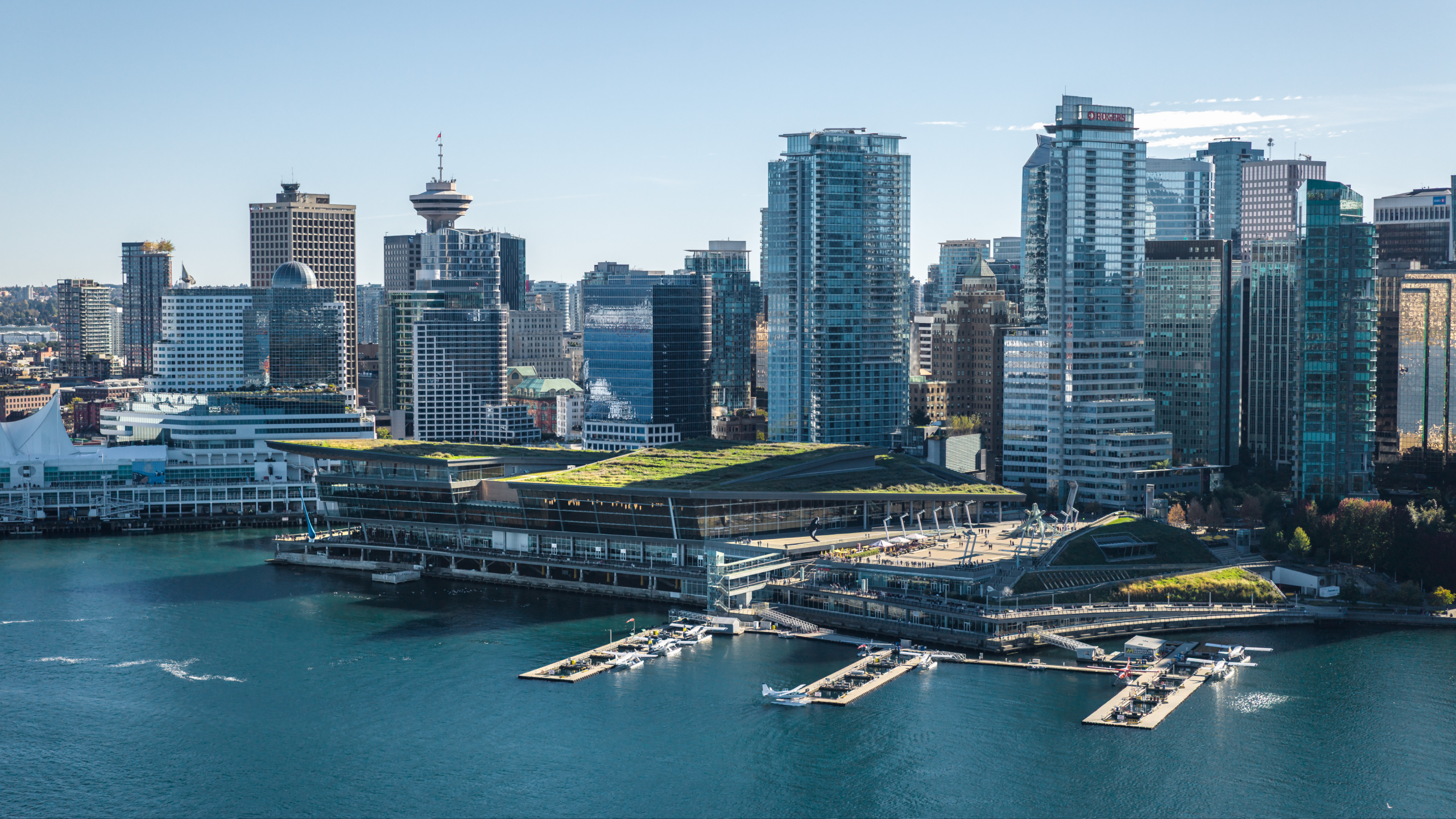 Waterfront city skyline with modern high-rise buildings and green-roofed structures by the harbor.