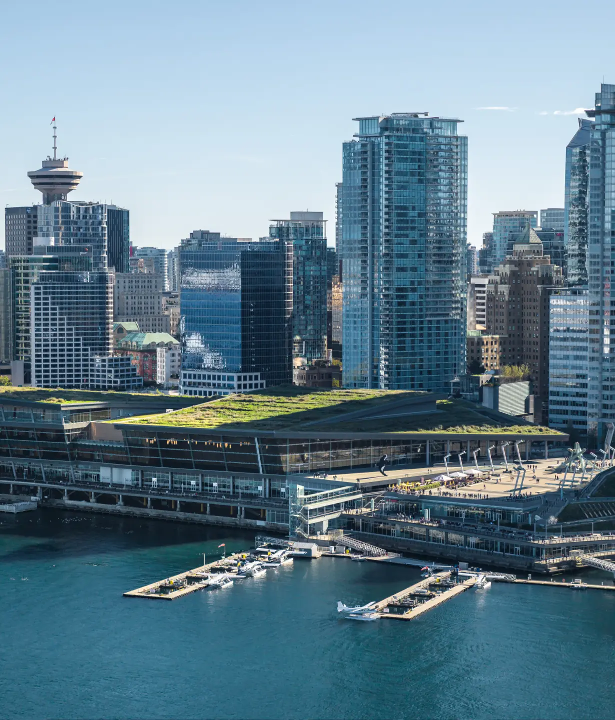 Waterfront city skyline with modern high-rise buildings and green-roofed structures by the harbor.