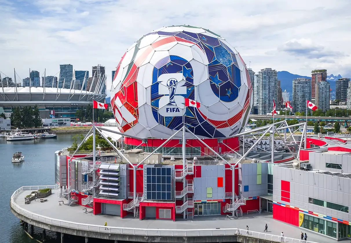 Large spherical structure with FIFA World Cup 2026 logo on a waterfront building with Canadian flags and city skyline in the background.