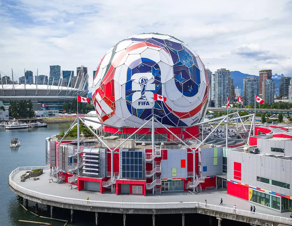 Large spherical structure with FIFA World Cup 2026 logo on a waterfront building with Canadian flags and city skyline in the background.