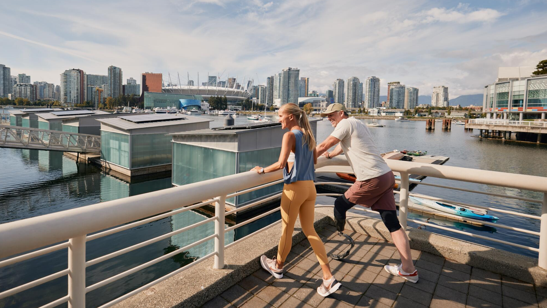 Two people stretching on a waterfront promenade with city skyline and boats in the background.