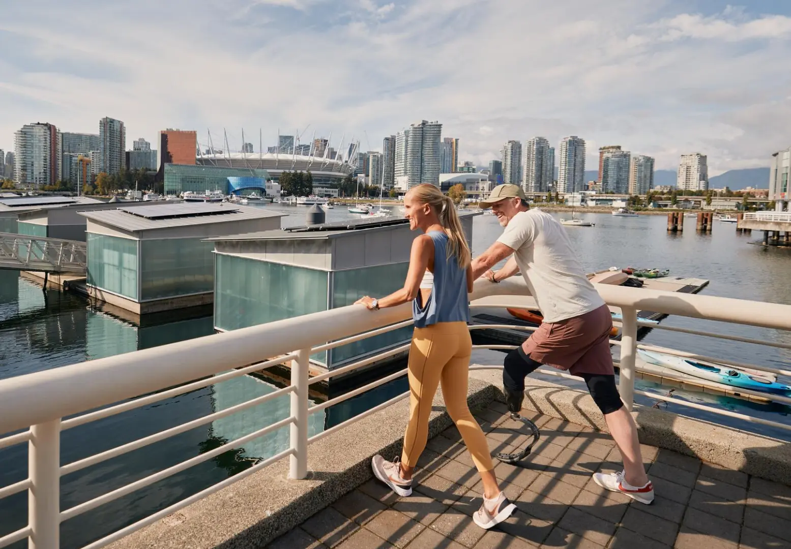 Two people stretching on a waterfront promenade with city skyline and boats in the background.