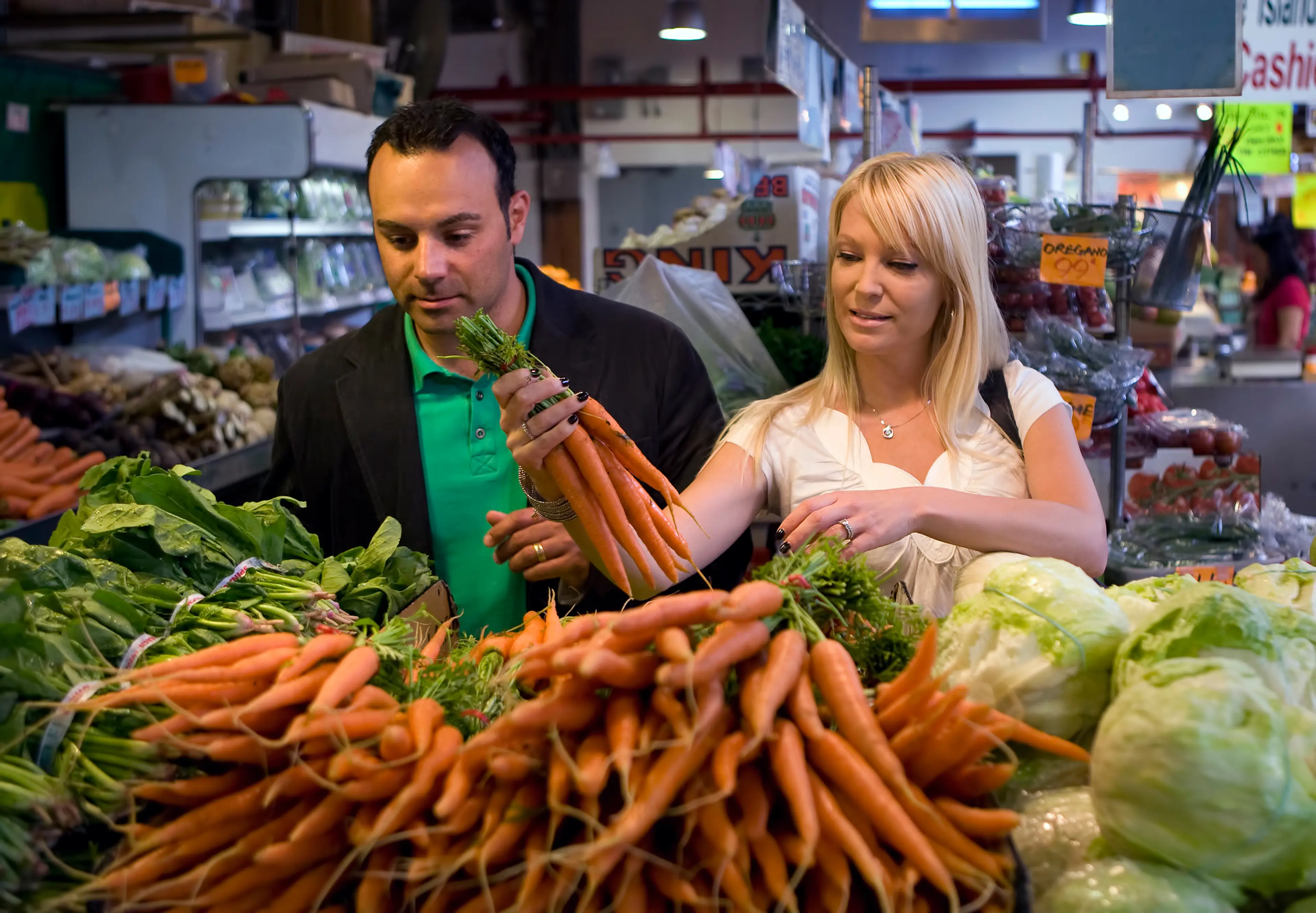 Two people shopping carrots at a produce stand in the Granville Island Public Market in Vancouver. 