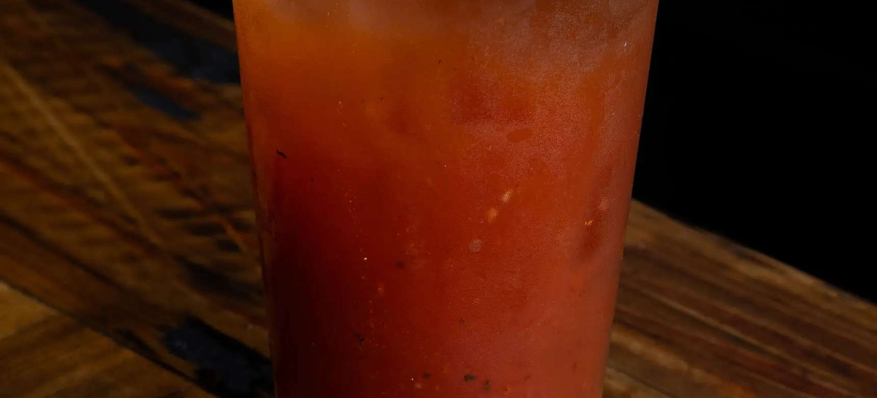 Bloody Mary cocktail garnished with lemon wedge, two green olives, and an oyster on a wooden table.