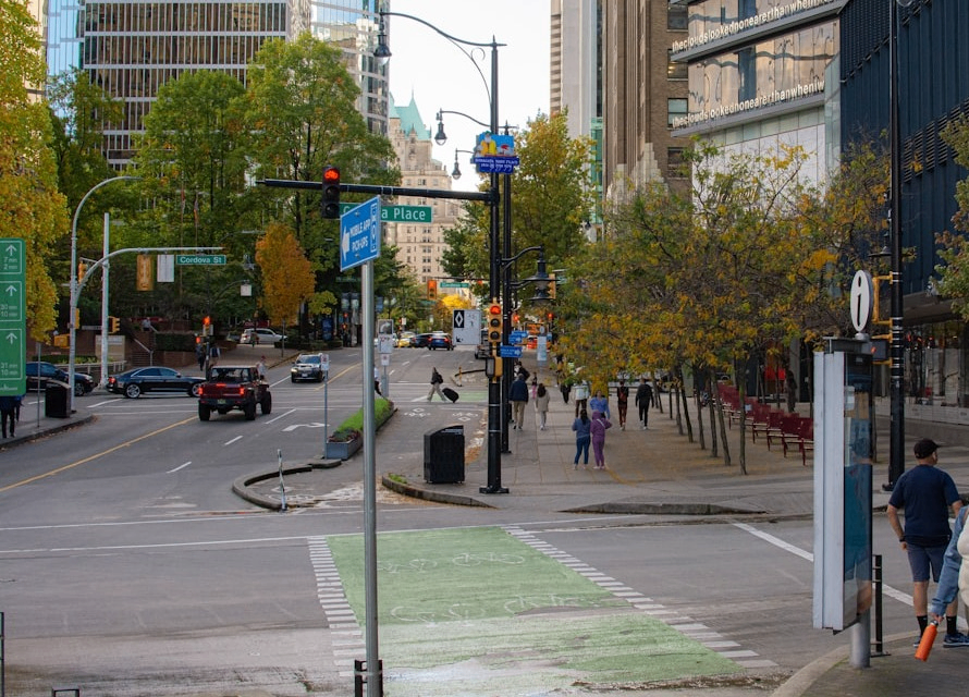 Urban street intersection with cars, pedestrians, green bike lane, and trees with autumn foliage.