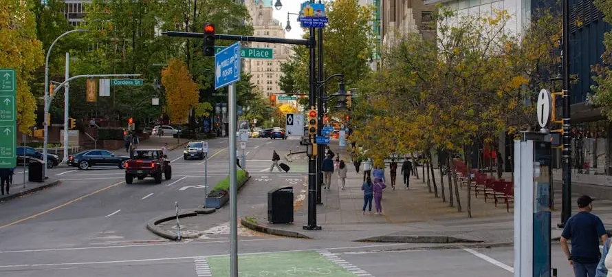Urban street intersection with cars, pedestrians, green bike lane, and trees with autumn foliage.