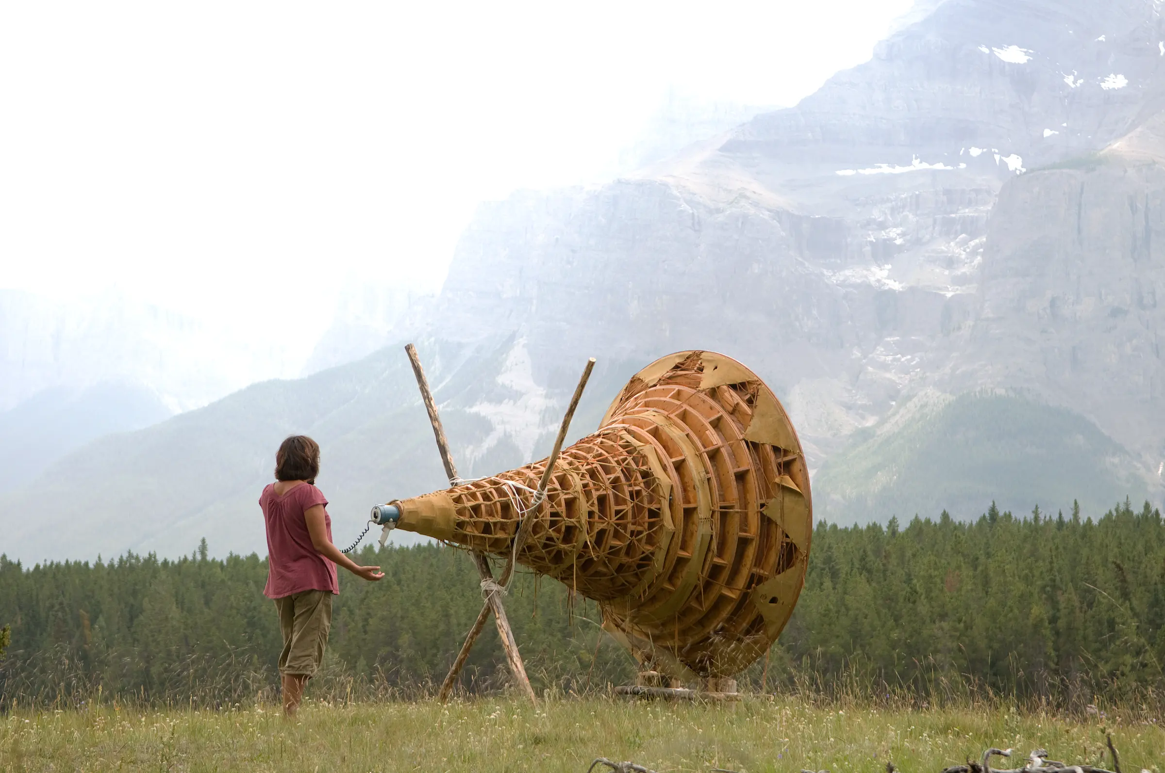Person standing in front of trees and mountain communicating through a large wooden device