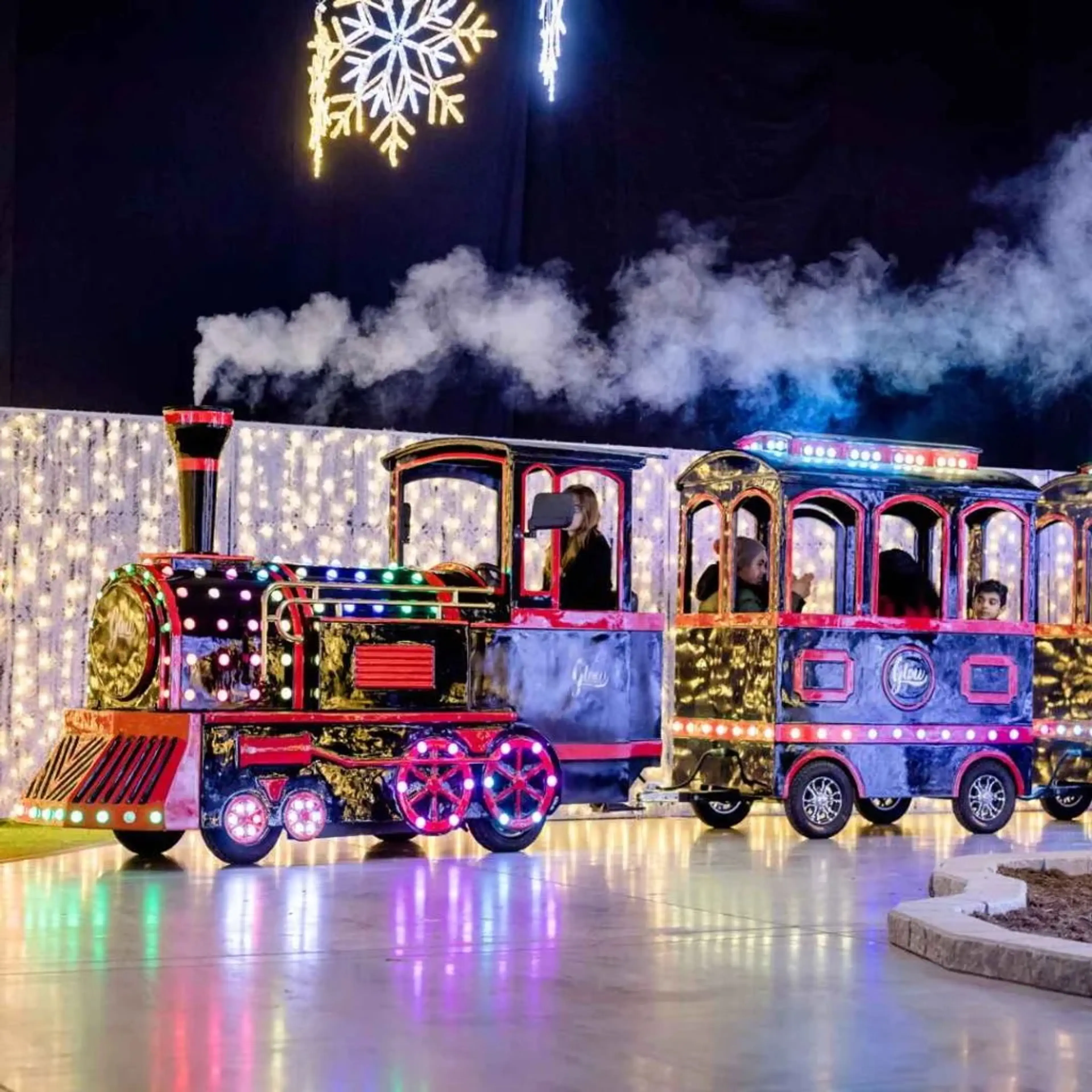 A mini-train covered in lights drives past holiday light displays at Glow Gardens Langley.