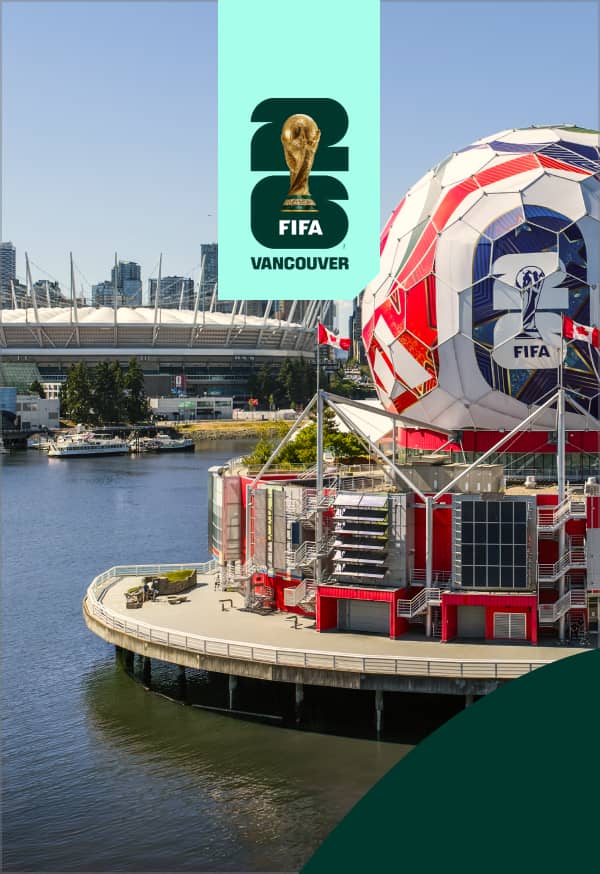 Large soccer ball structure with FIFA 2026 logo on waterfront in Vancouver, with stadium and city skyline in background.