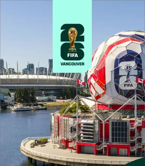 Large soccer ball structure with FIFA 2026 logo on waterfront in Vancouver, with stadium and city skyline in background.