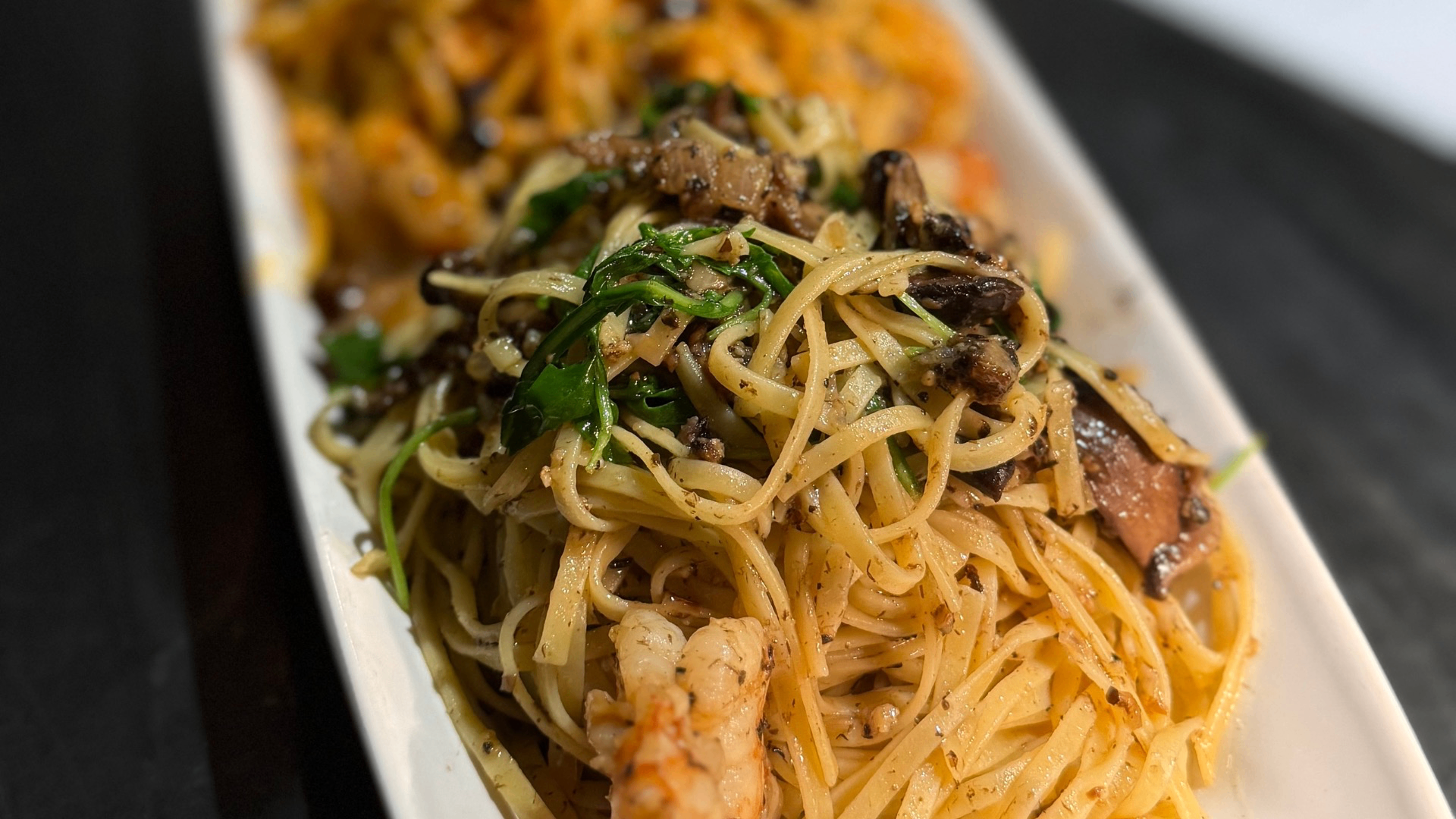 Plate of pasta with shrimp, mushrooms, and greens on a white rectangular dish.
