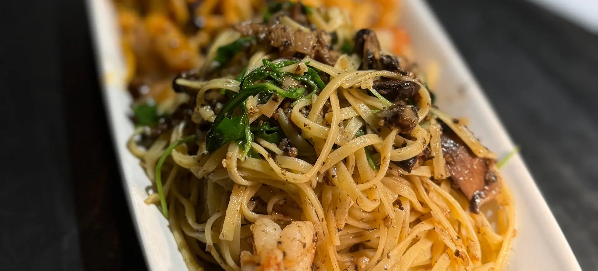 Plate of pasta with shrimp, mushrooms, and greens on a white rectangular dish.