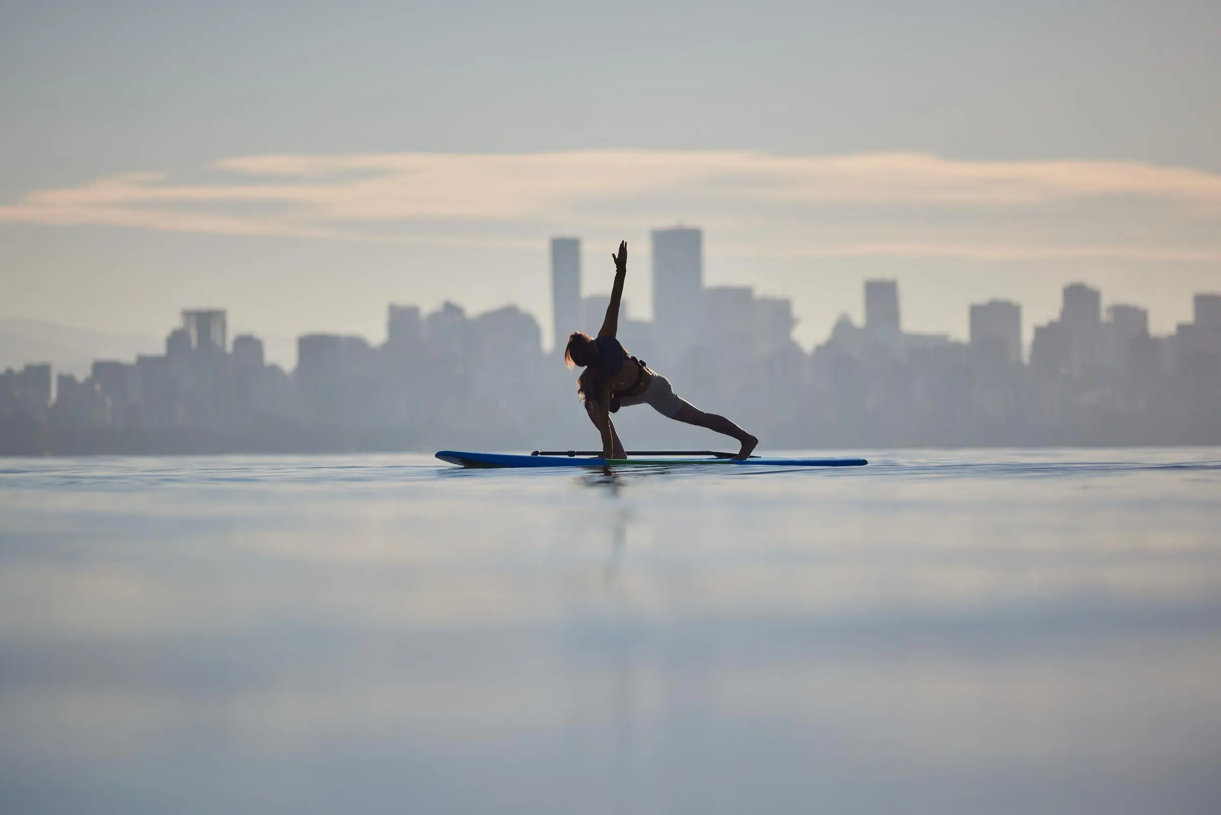 A person doing paddle board yoga with Vancouver's downtown in the background.