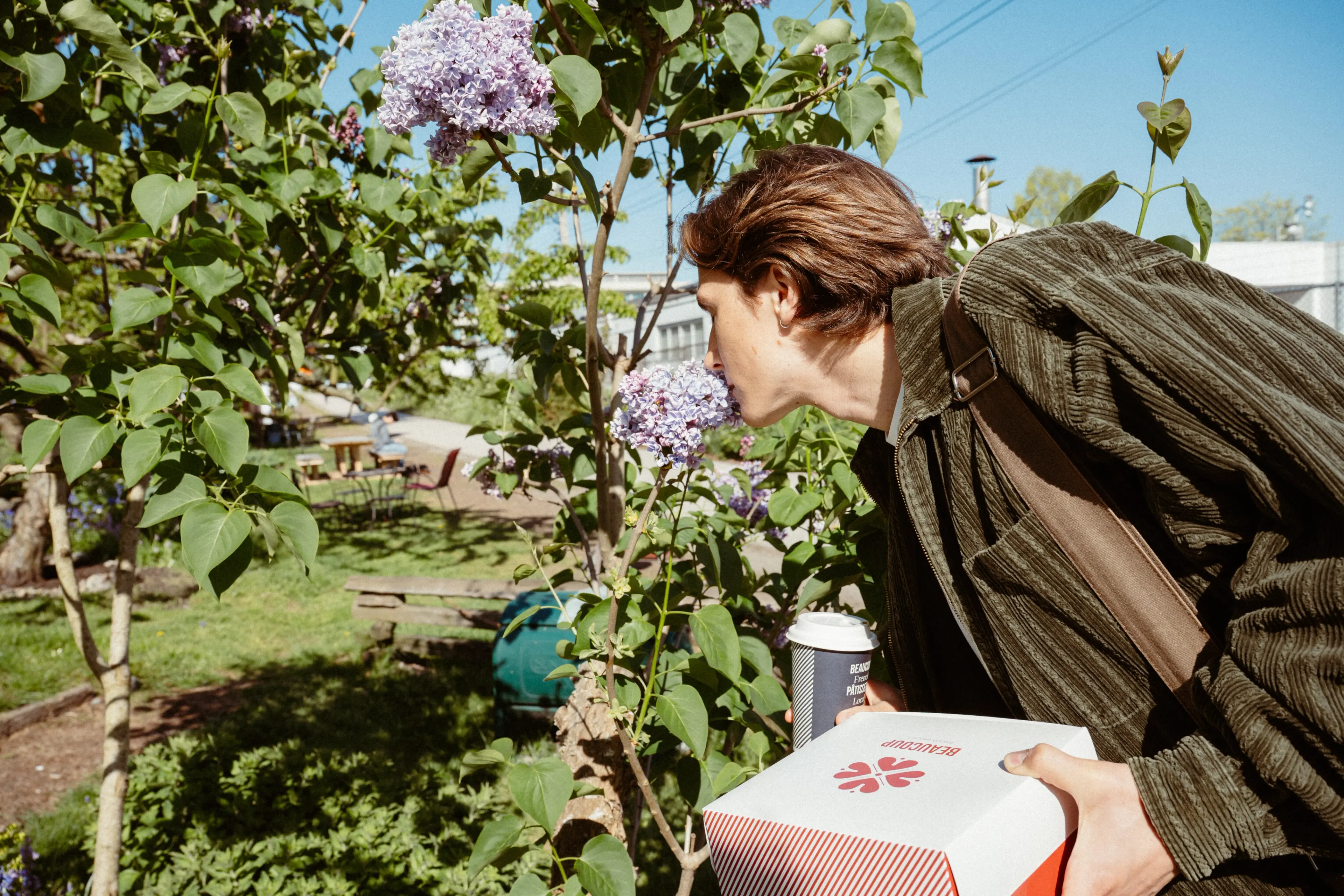 Someone stopping to smell the flowers on the Arbutus Greenway with a box of Beaucoup Bakery treats
