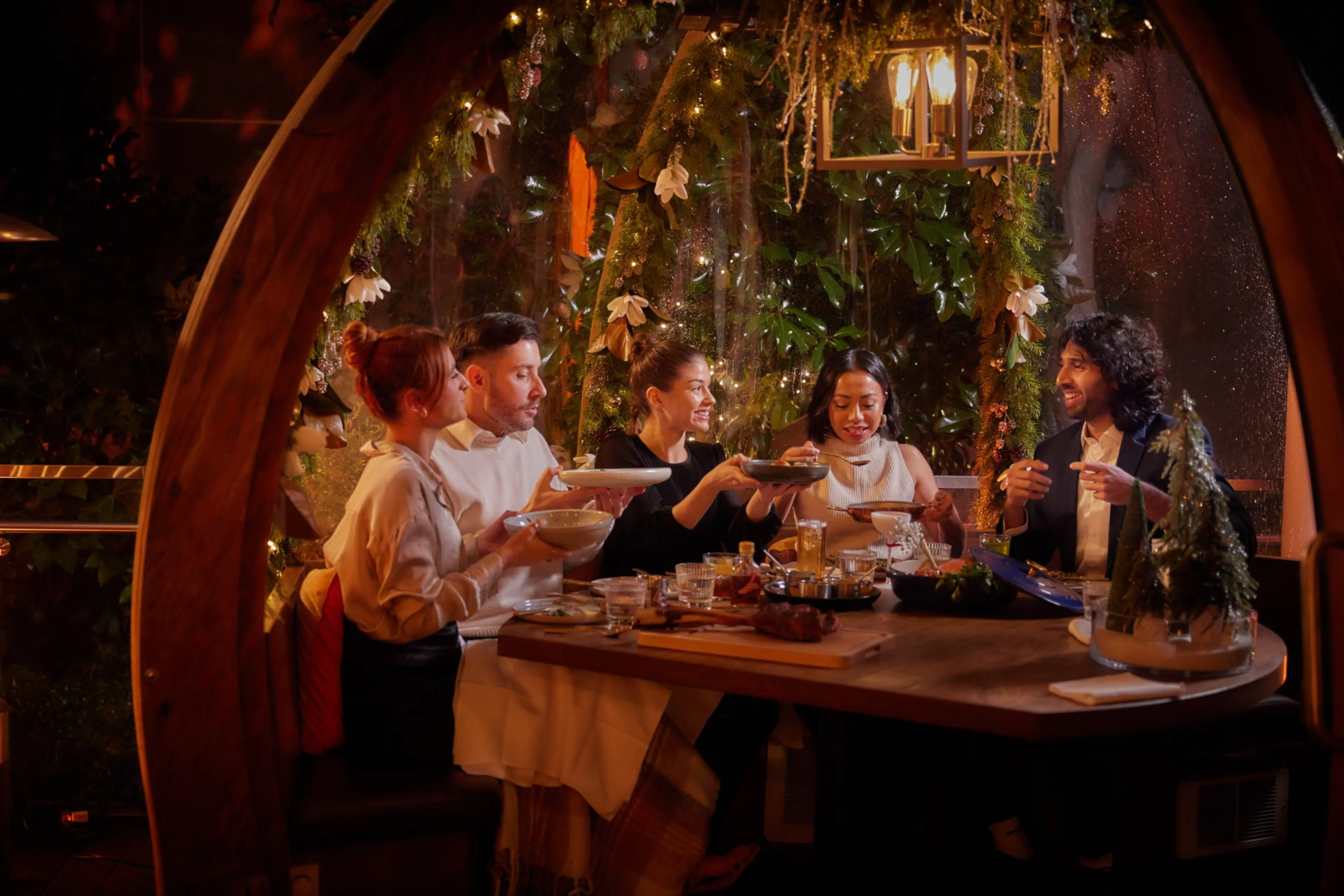 Four people enjoy food and drinks inside a translucent dome with holiday decorations at the Winterlust event at the H Tasting Lounge in Vancouver.