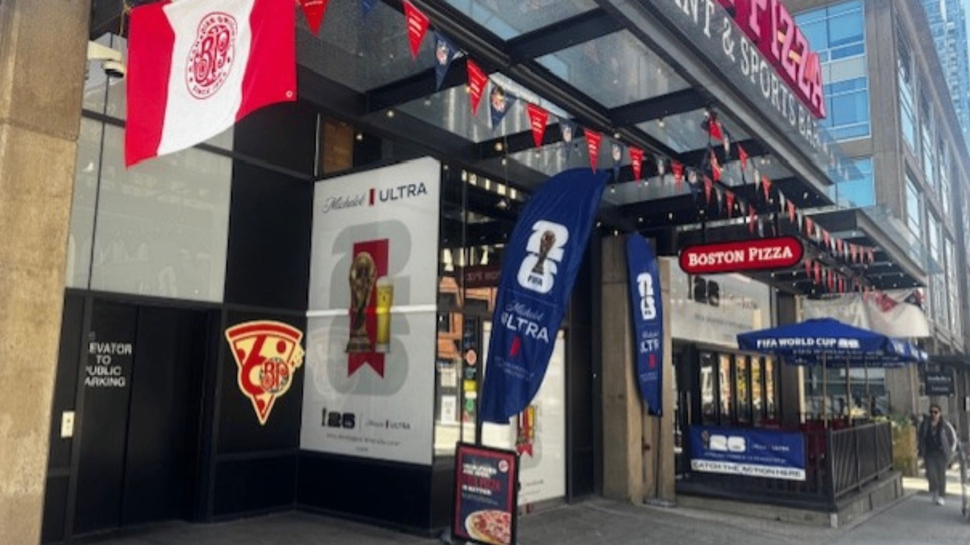 Exterior of Boston Pizza restaurant decorated with banners and flags for FIFA World Cup and Michelob Ultra.