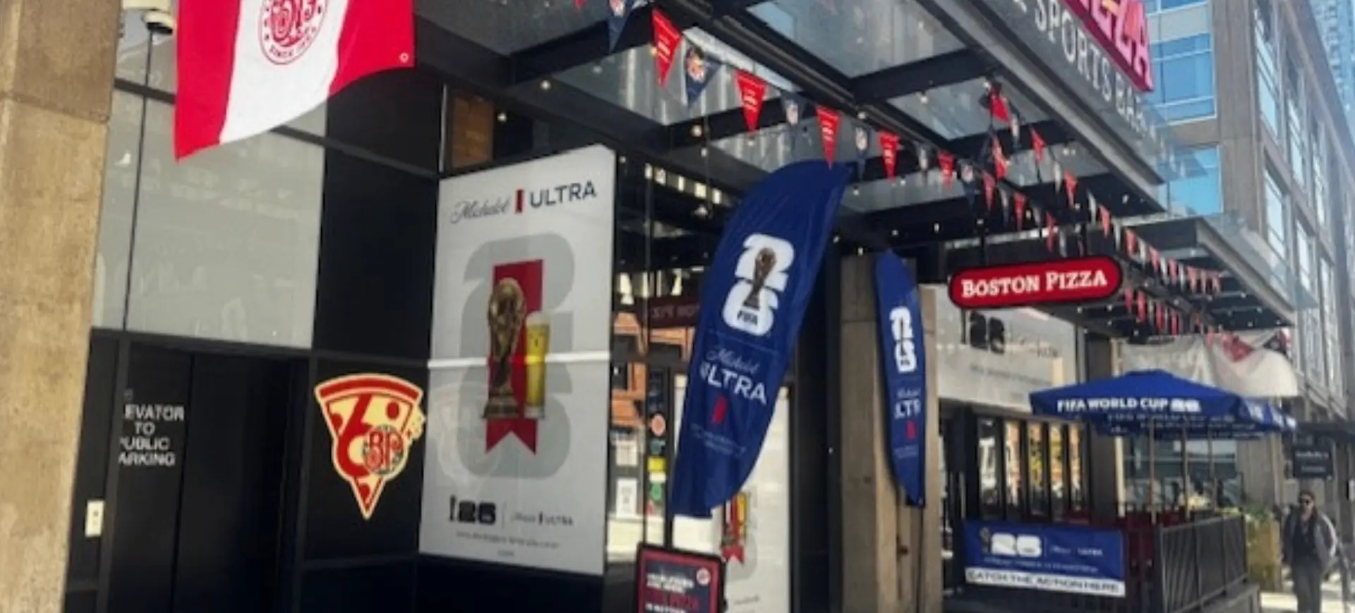 Exterior of Boston Pizza restaurant decorated with banners and flags for FIFA World Cup and Michelob Ultra.