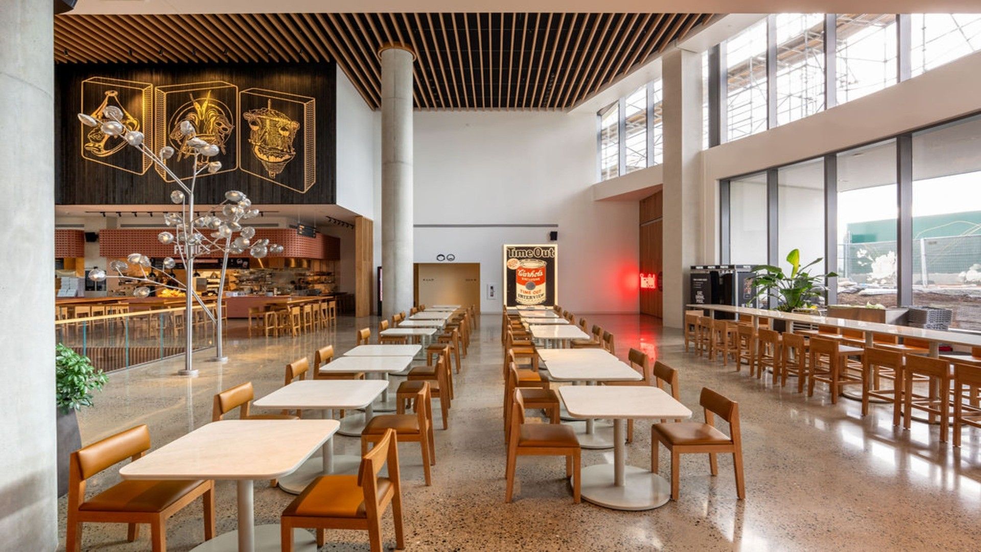 Empty modern cafeteria with rows of tables and chairs, large windows on the right, and decorative light fixtures.