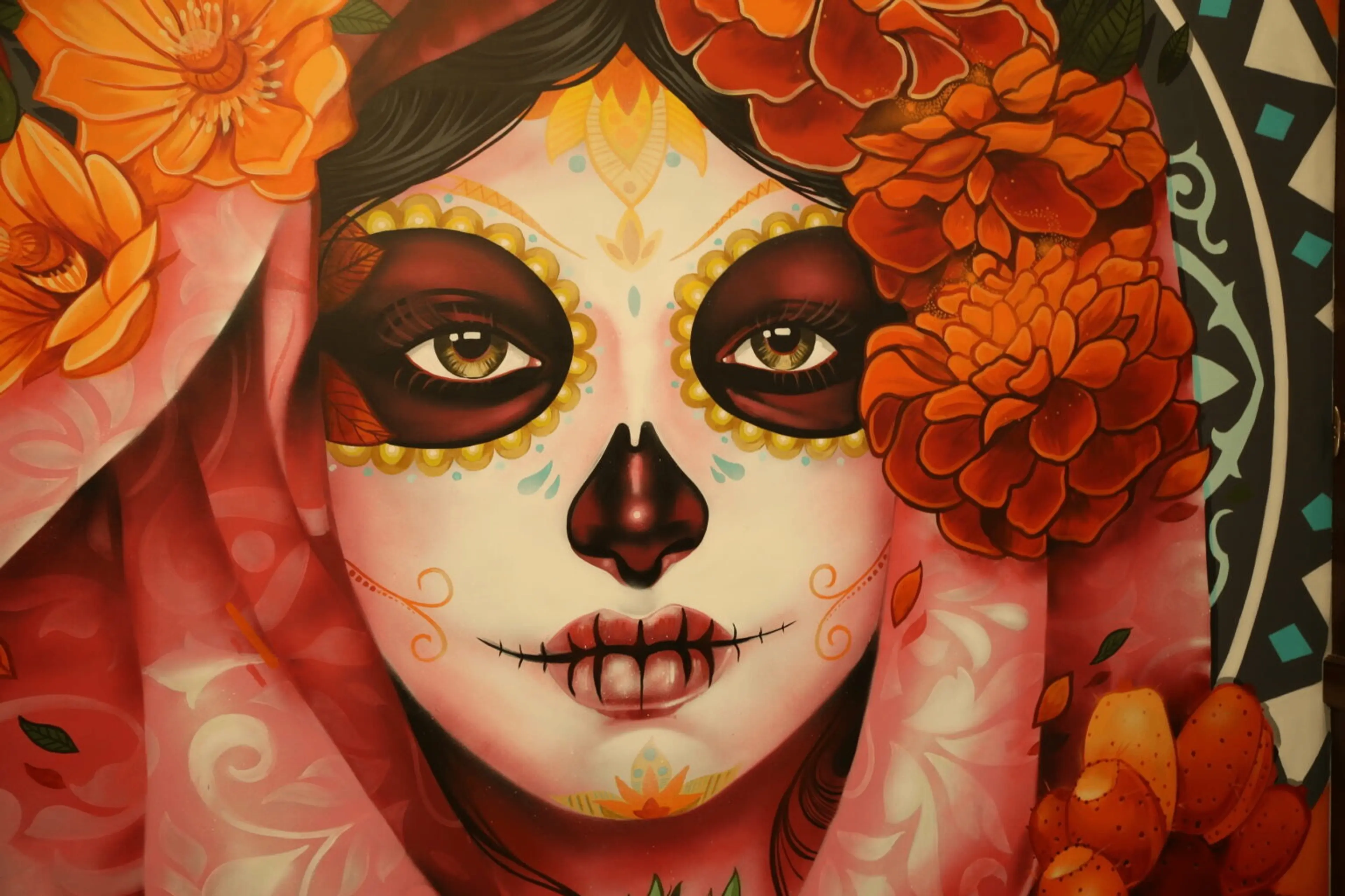 Face painted with Day of the Dead makeup surrounded by orange flowers and a pink patterned shawl.