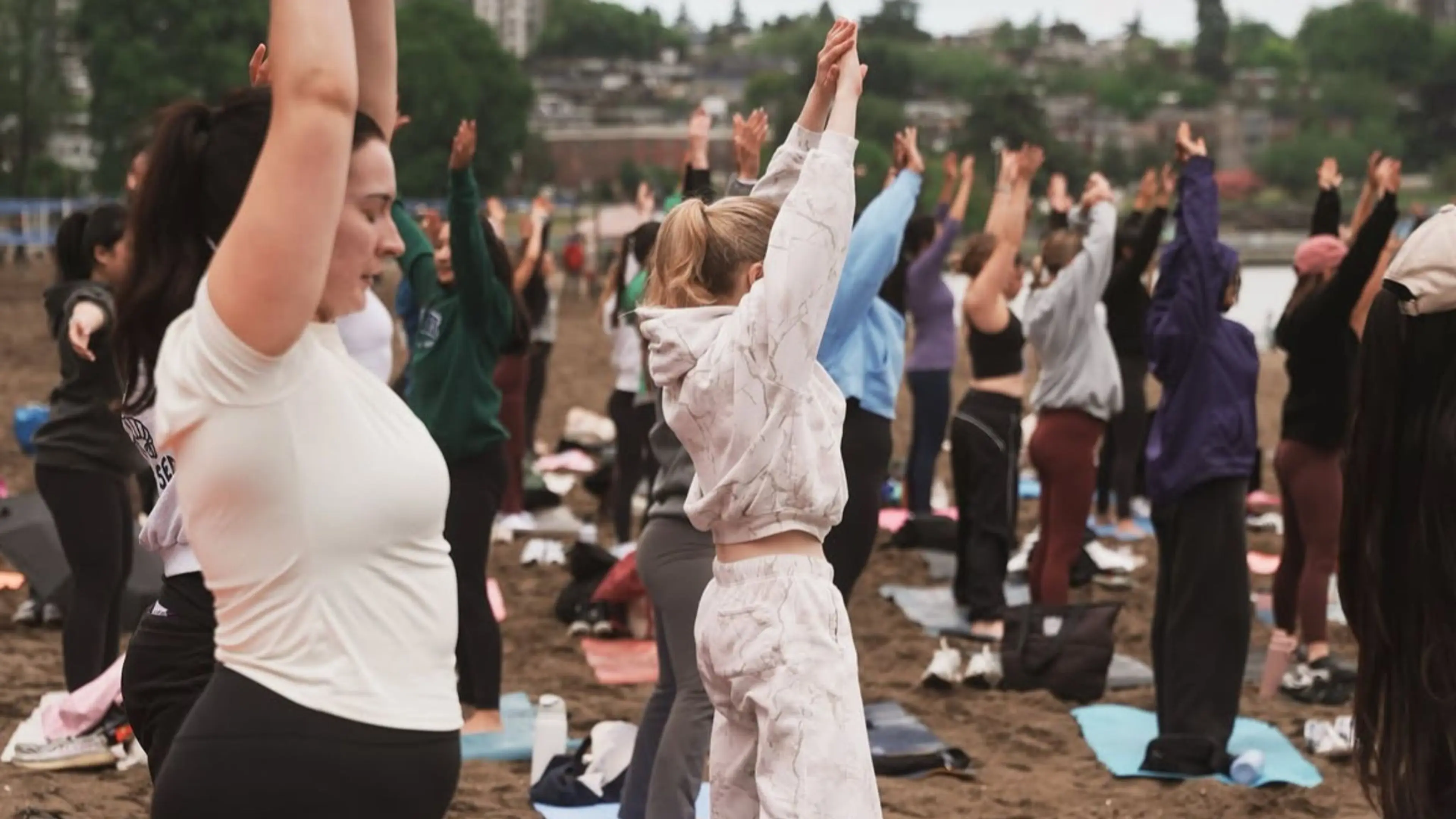 A group of people standing on mats outdoors with arms raised, participating in a group exercise or yoga session.
